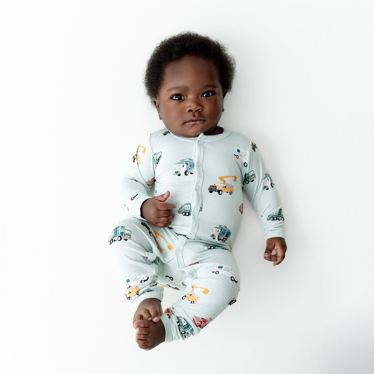Infant lying on a white surface wearing the soft and breathable Romper in City Vehicles