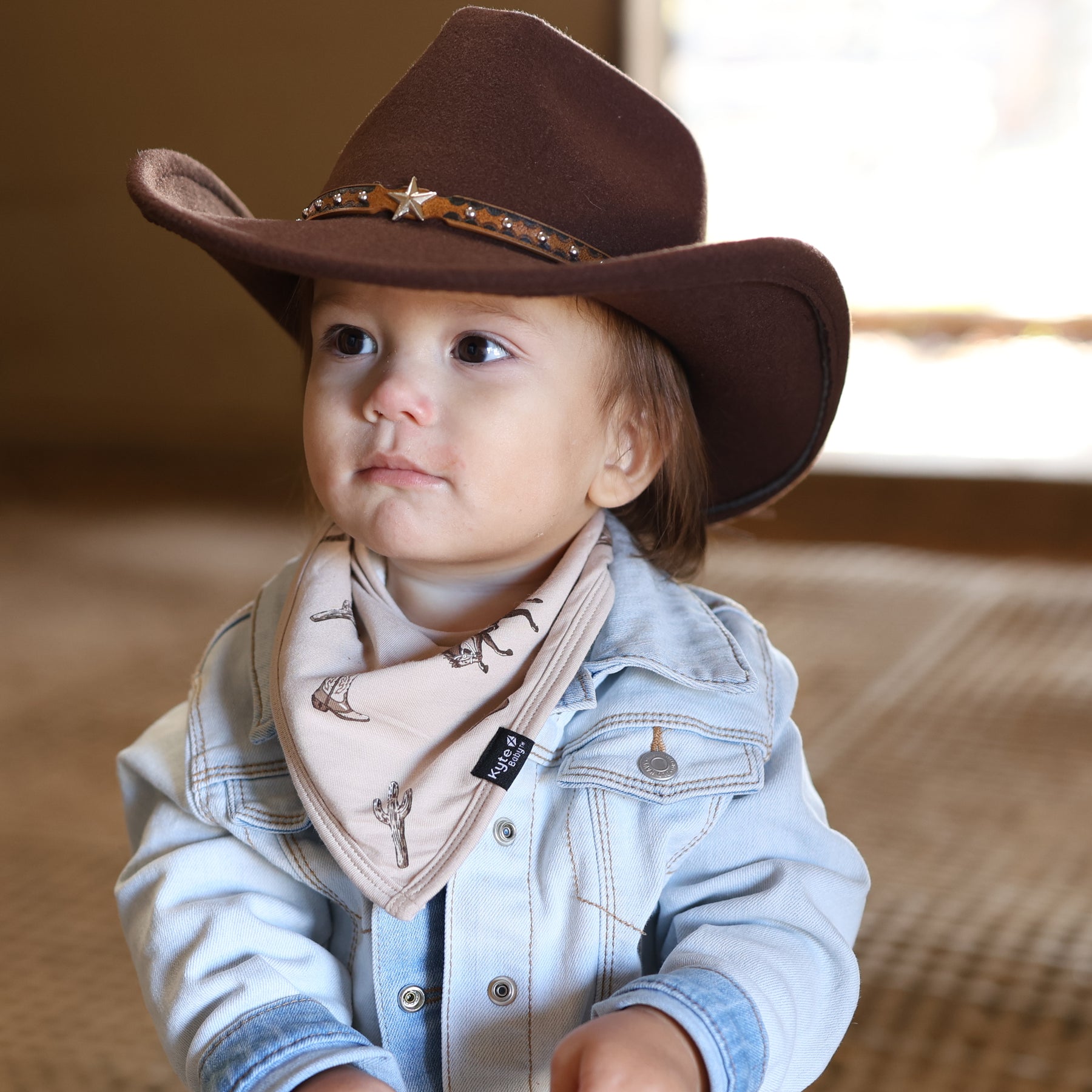Close up of toddler wearing the Bib in Classic Cowboy paired with a brown cowboy hat and light wash jean jacket