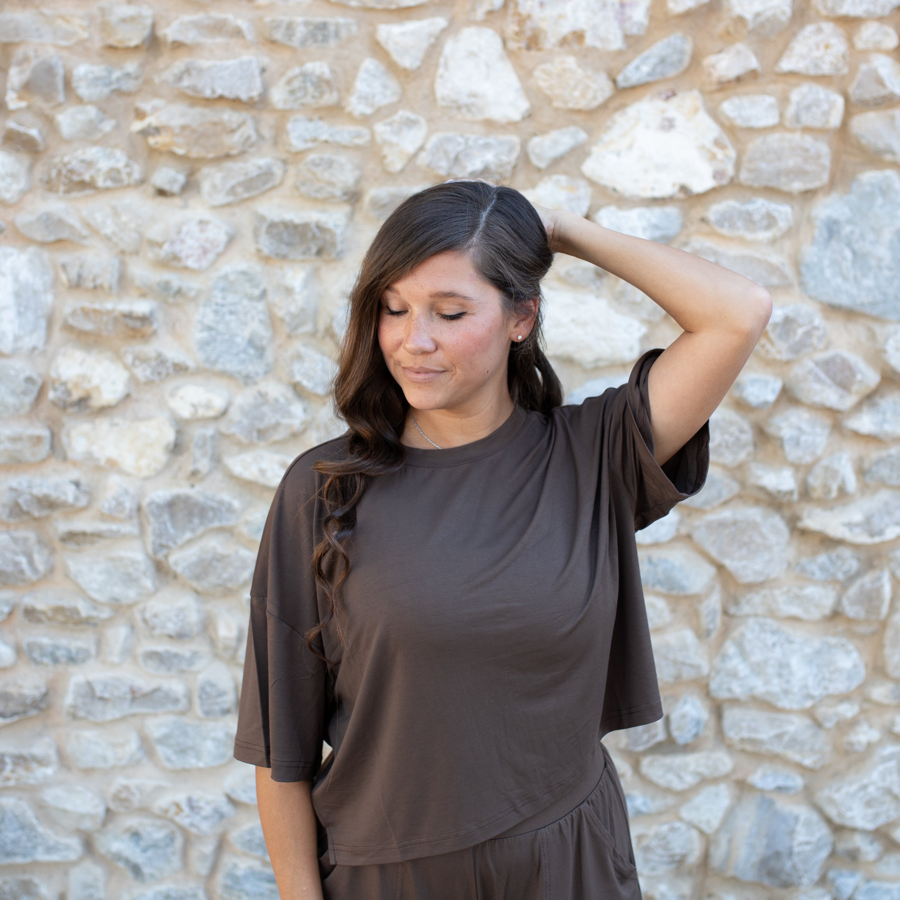 Woman wearing a brown top standing in front of a stone wall