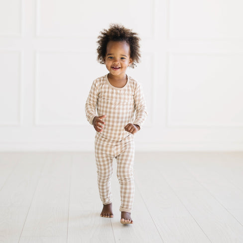 Young toddler walking wearing the Long Sleeve Pajamas in Gingham Bisque