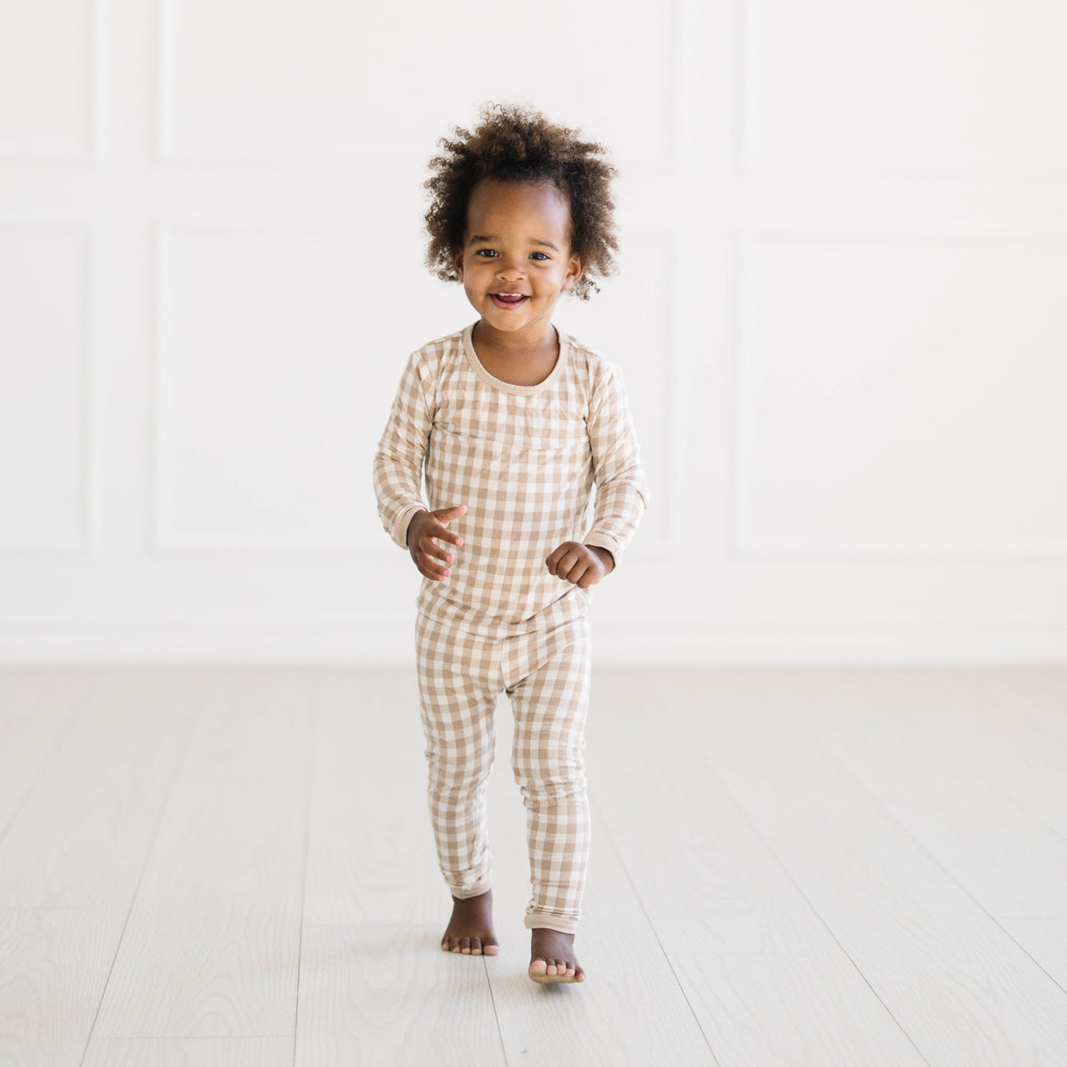 Young toddler walking wearing the Long Sleeve Pajamas in Gingham Bisque