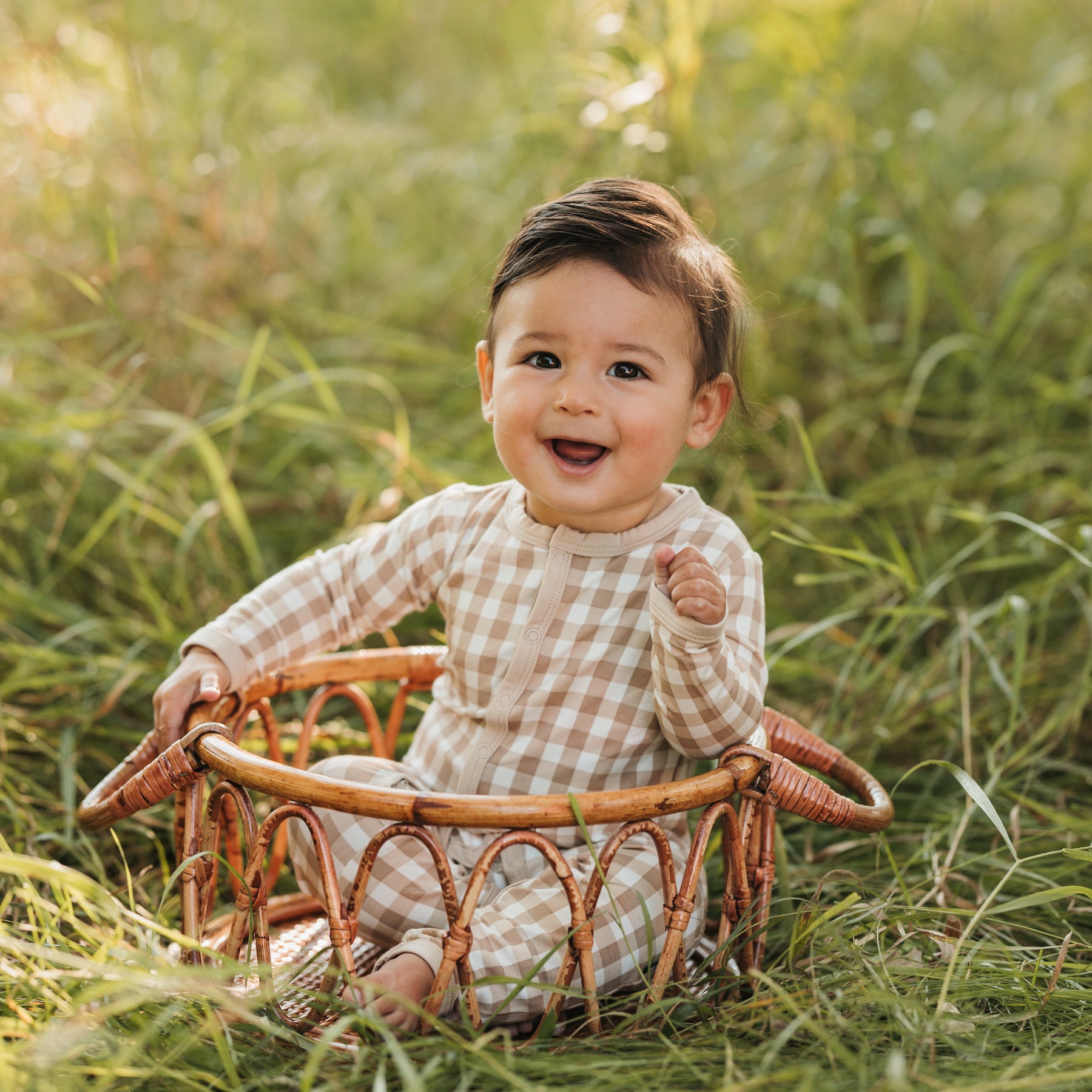 Infant sitting in a wicker basket in the grass wearing the Romper in Gingham Bisque