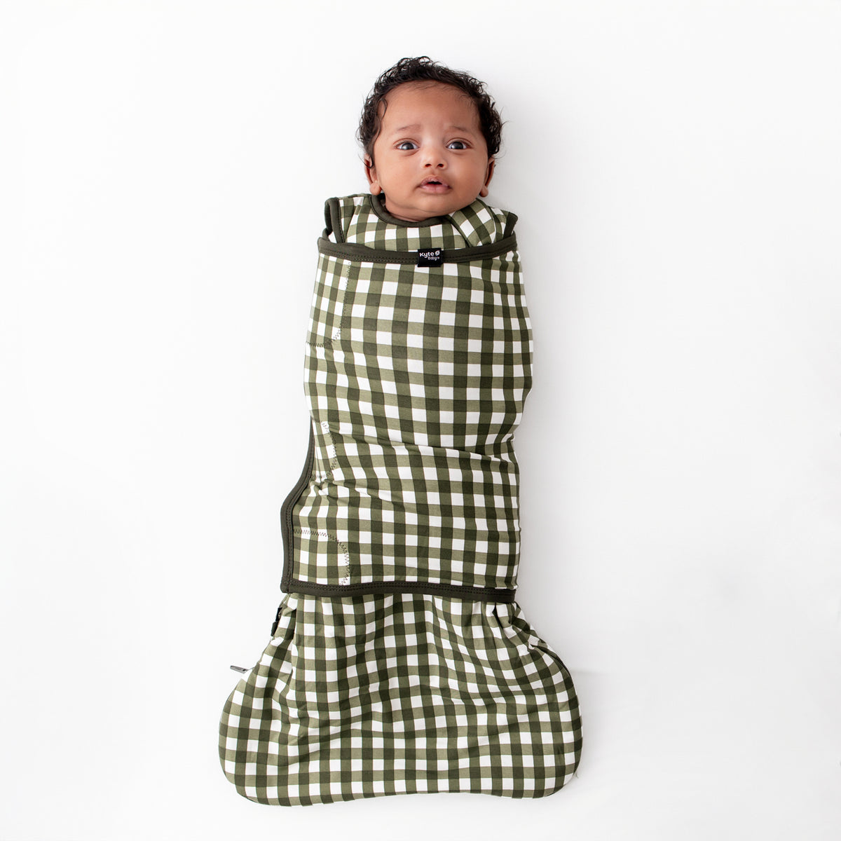 Infant laying down shown swaddled in the Sleep Bag Swaddler in Gingham Fir 1.0