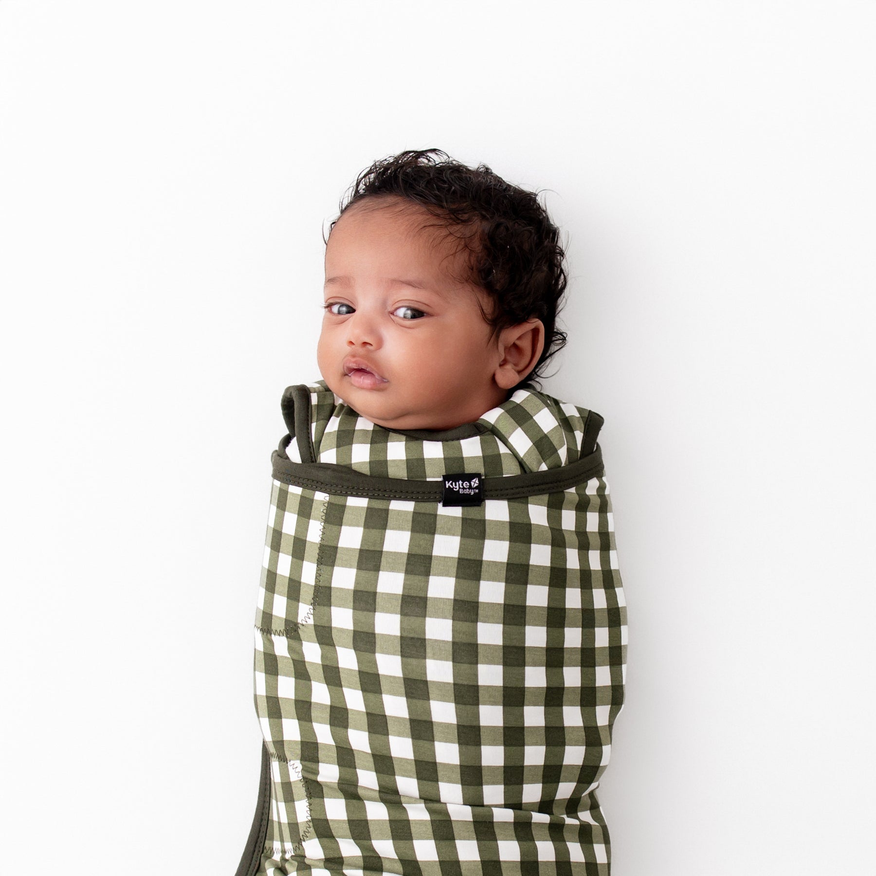 Close up of the Sleep Bag Swaddler in Gingham Fir 1.0 shown on a swaddled infant
