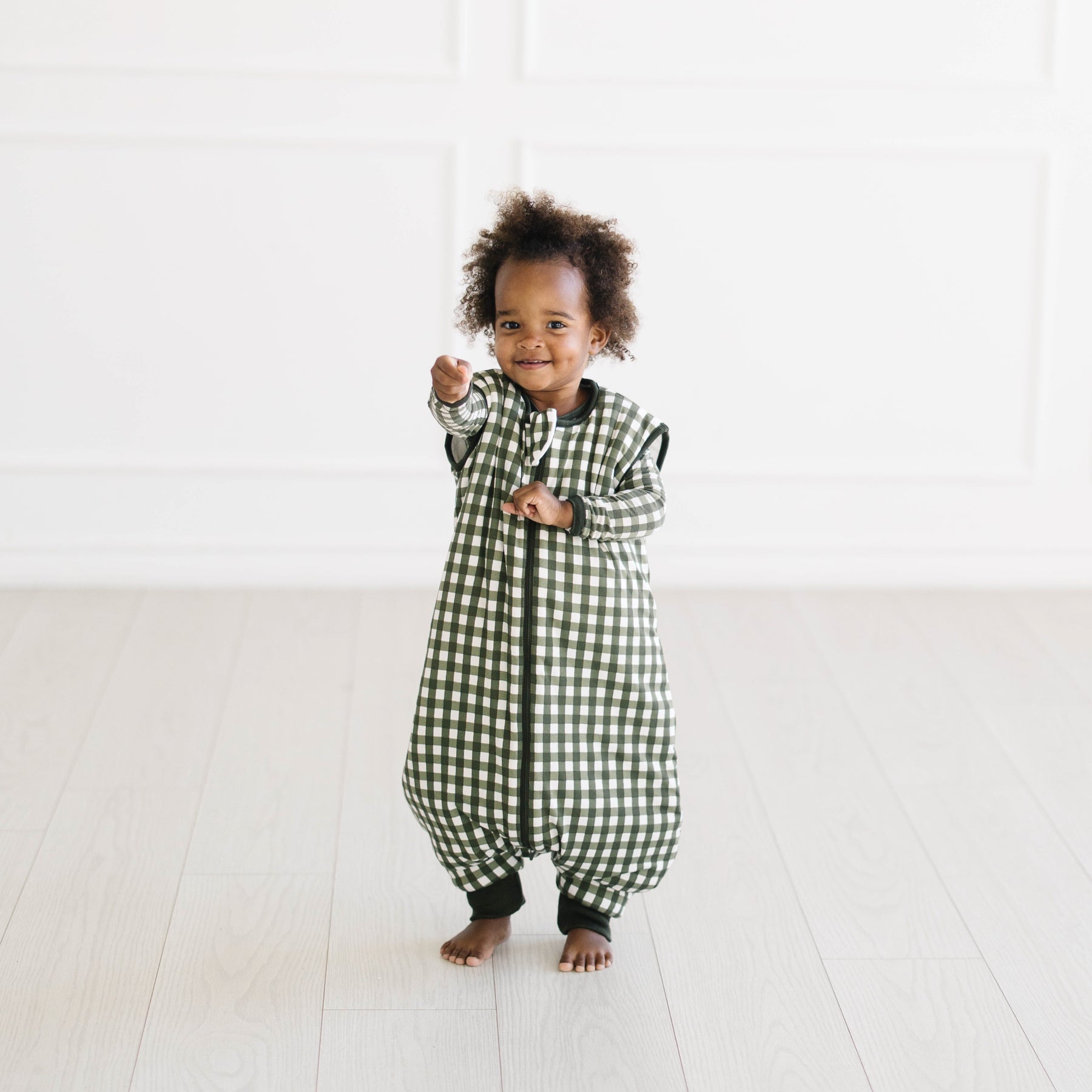 Young toddler standing wearing the Sleep Bag Walker in Gingham Fir 2.5 with matching long sleeve toddler pajamas on underneath