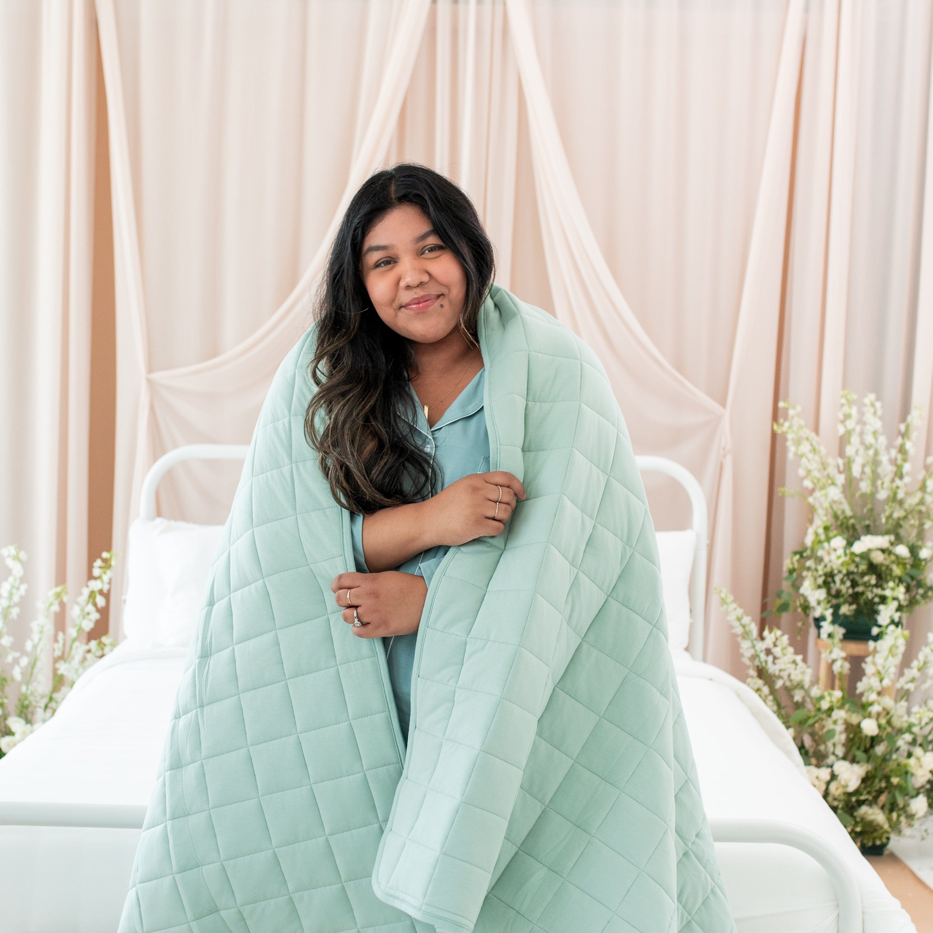 Woman wrapped in Kyte Baby Adult Quilted Twin Blanket in Sage 3.5