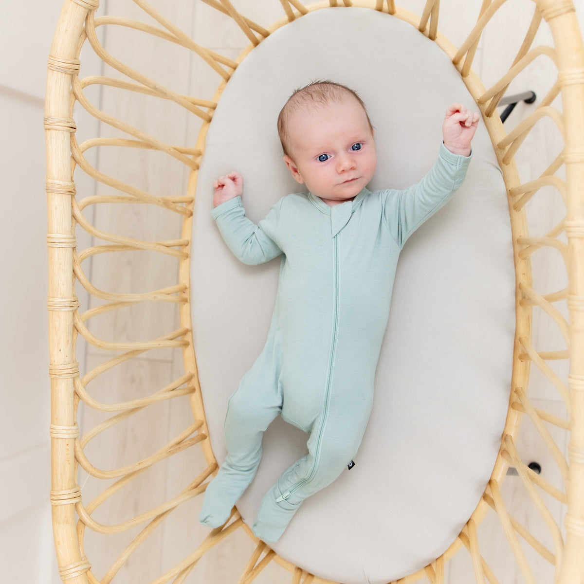 Baby laying on Kyte Baby Oval Bassinet Sheet in Oat