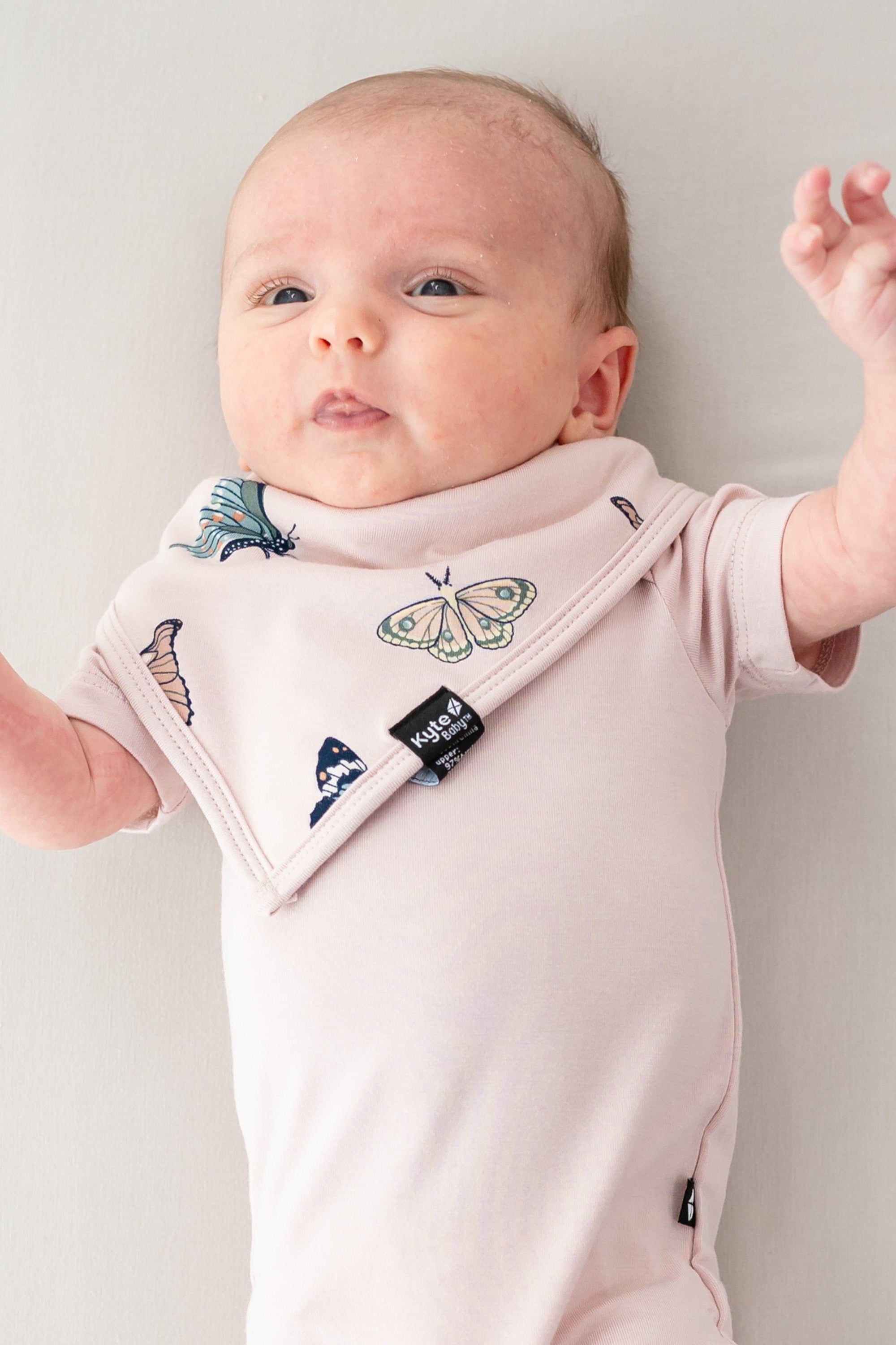 Infant laying down with hands in the air wearing the Bib in Blush Butterfly and Blush short sleeve bodysuit