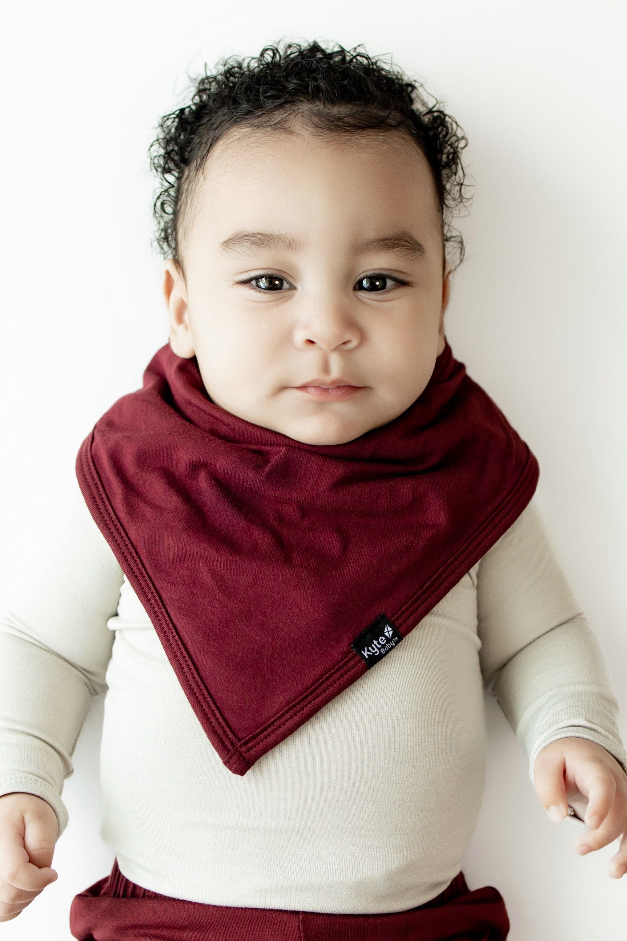 Infant wearing the Bib in Burgundy overtop an Oat long sleeve bodysuit