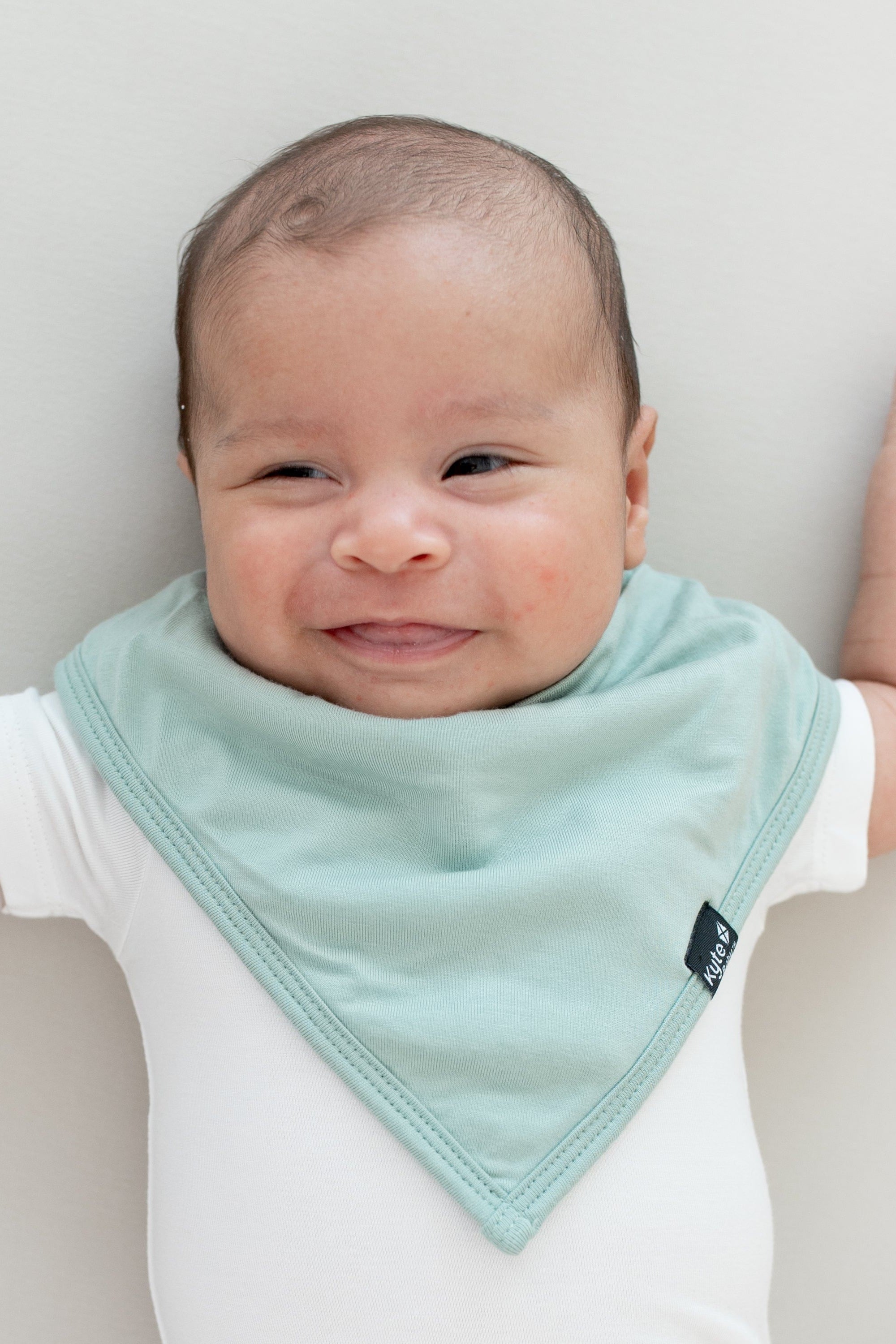 Smiling infant wearing the Kyte Baby Bib Sage and Short Sleeve Bodysuit in Cloud