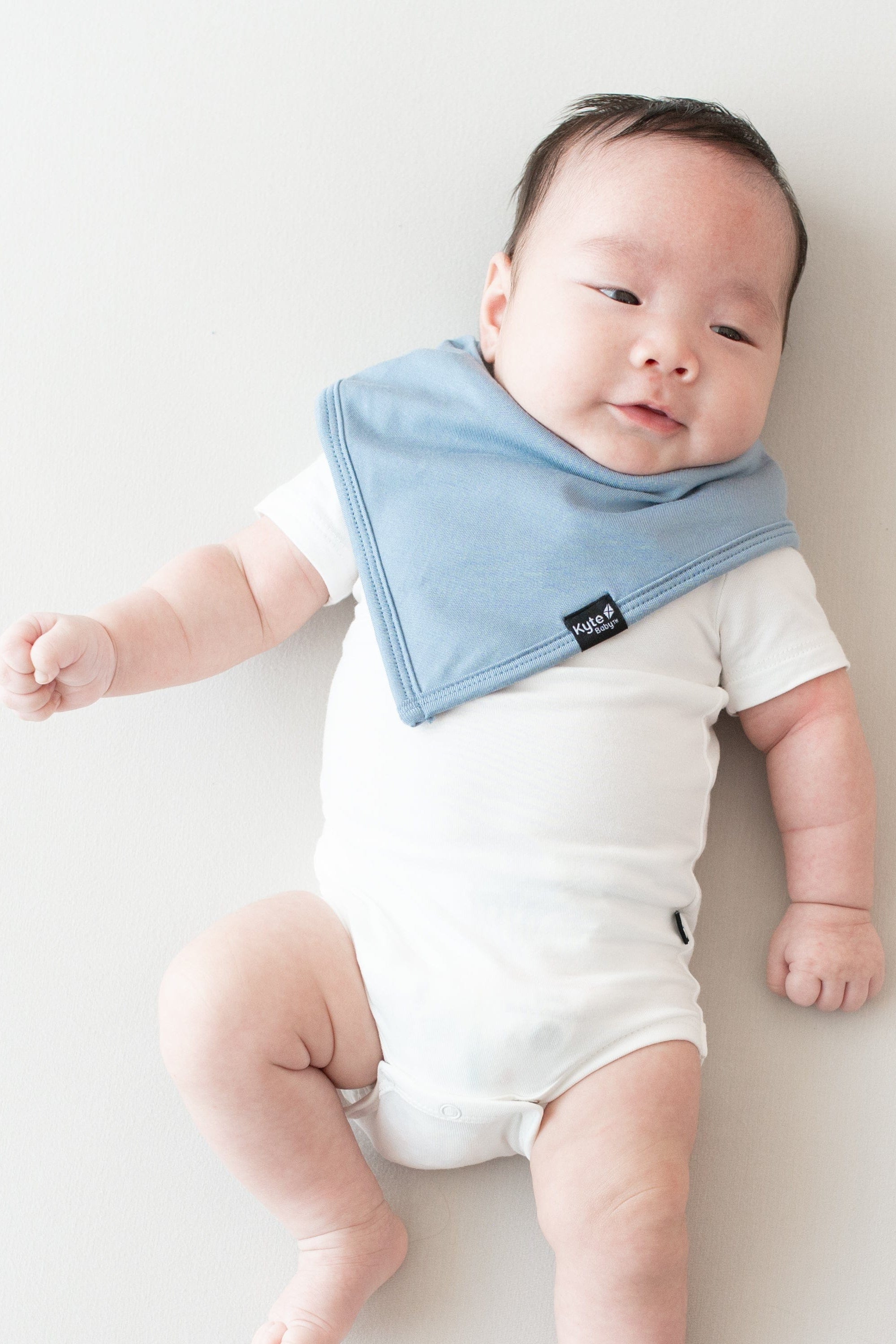 Baby laying on an oat surface while wearing a Bib in Slate