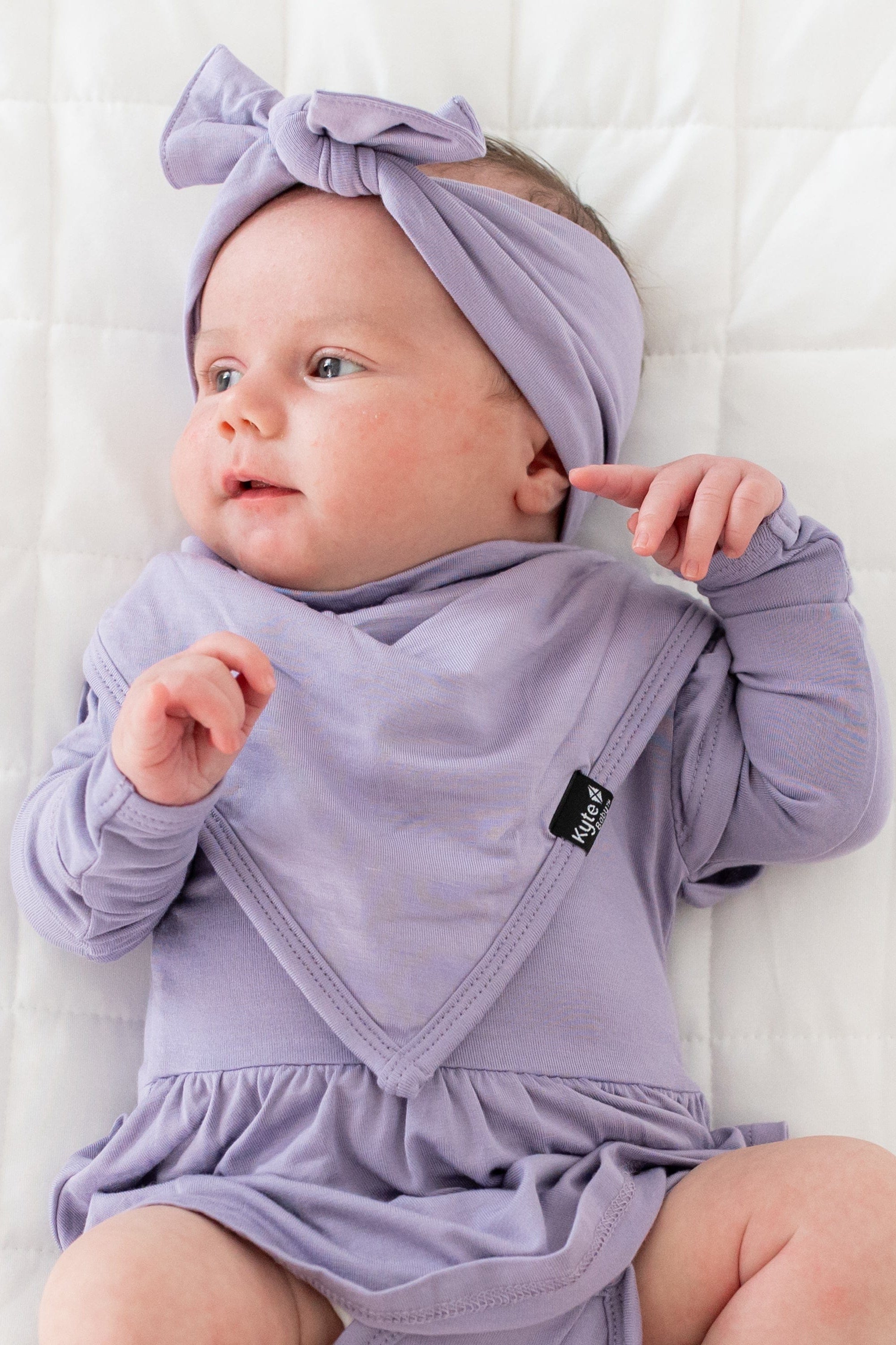 Baby wearing a bib in Taro with matching Twirl Bodsyuit and Bow