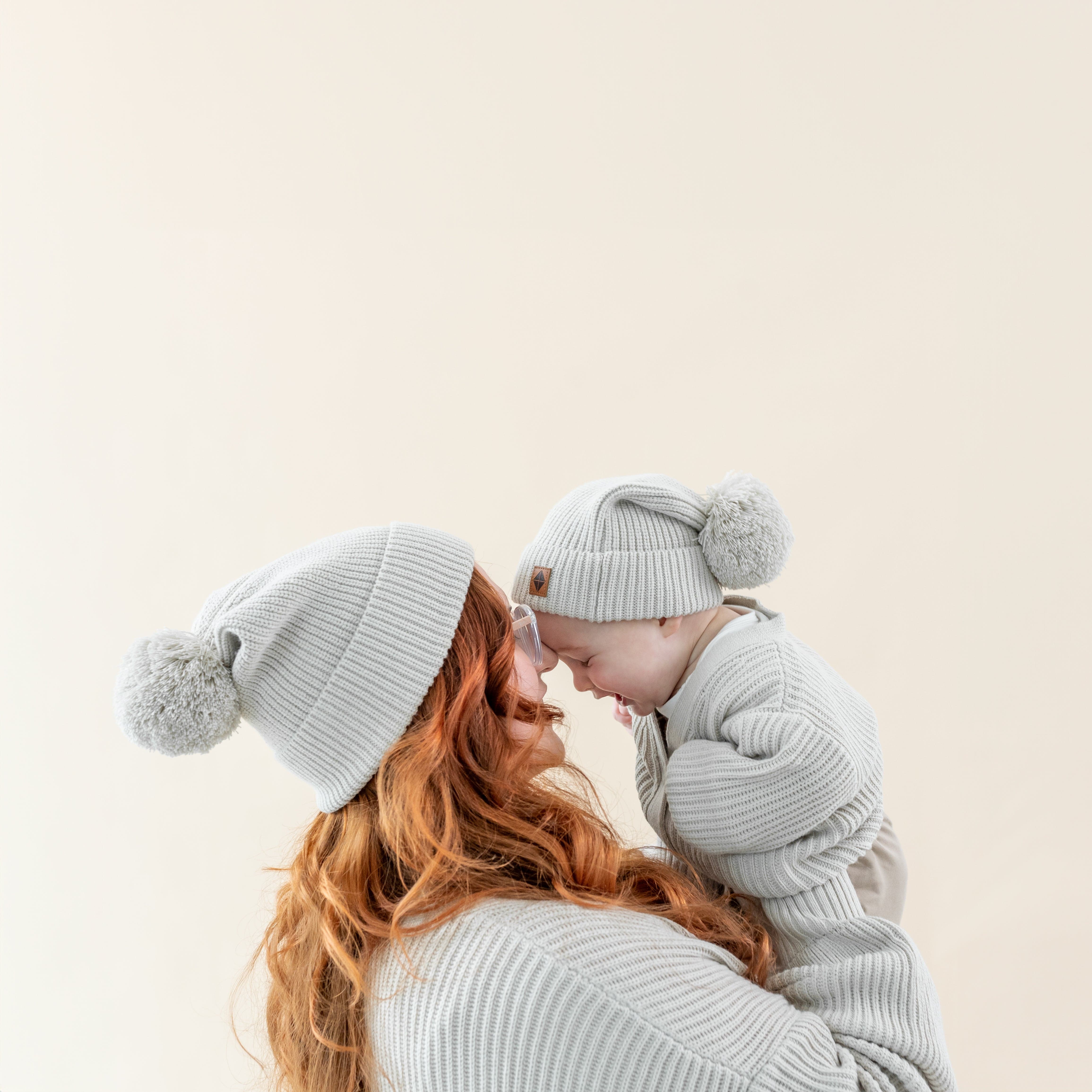Mom and child wearing matching Kyte Baby Chunky Knit Beanies with Pom Detail in Oat