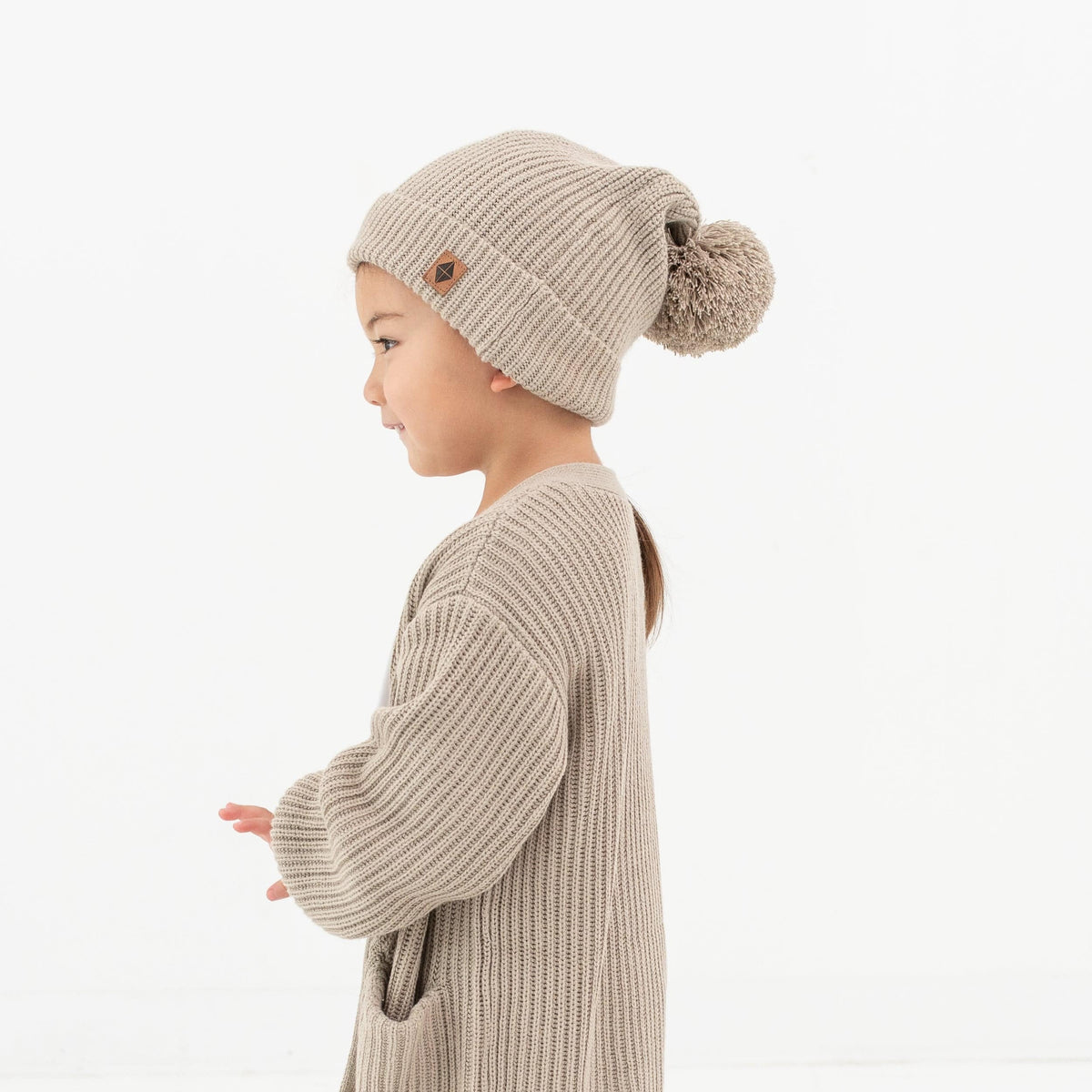 Child wearing Kyte Baby Chunky Knit Pom Beanie in Almond