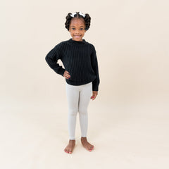 Child wearing Kyte Baby Ribbed Leggings in Oat with Chunky Knit Sweater in Midnight