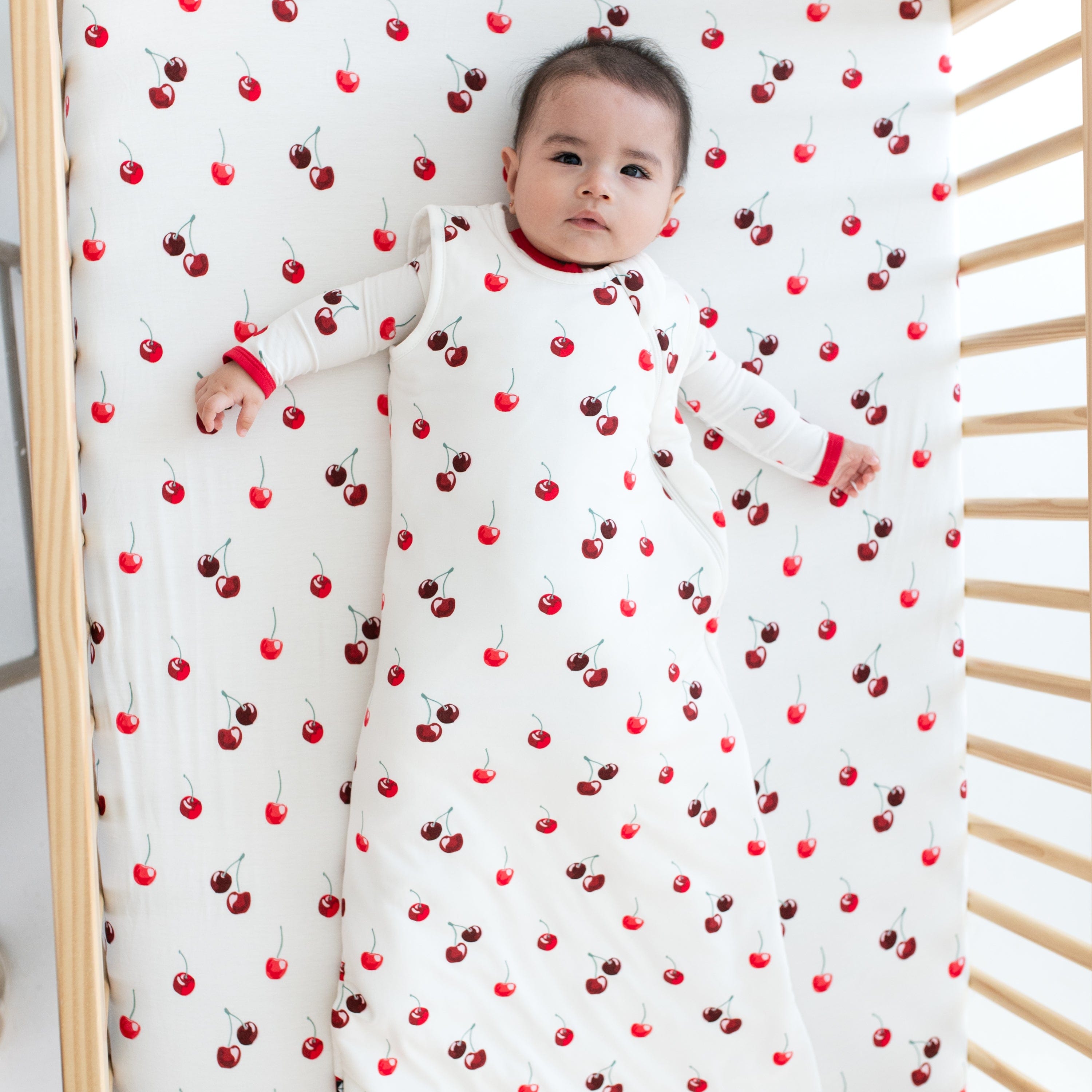 Baby laying on Kyte Baby Crib Sheet in Cherry pattern