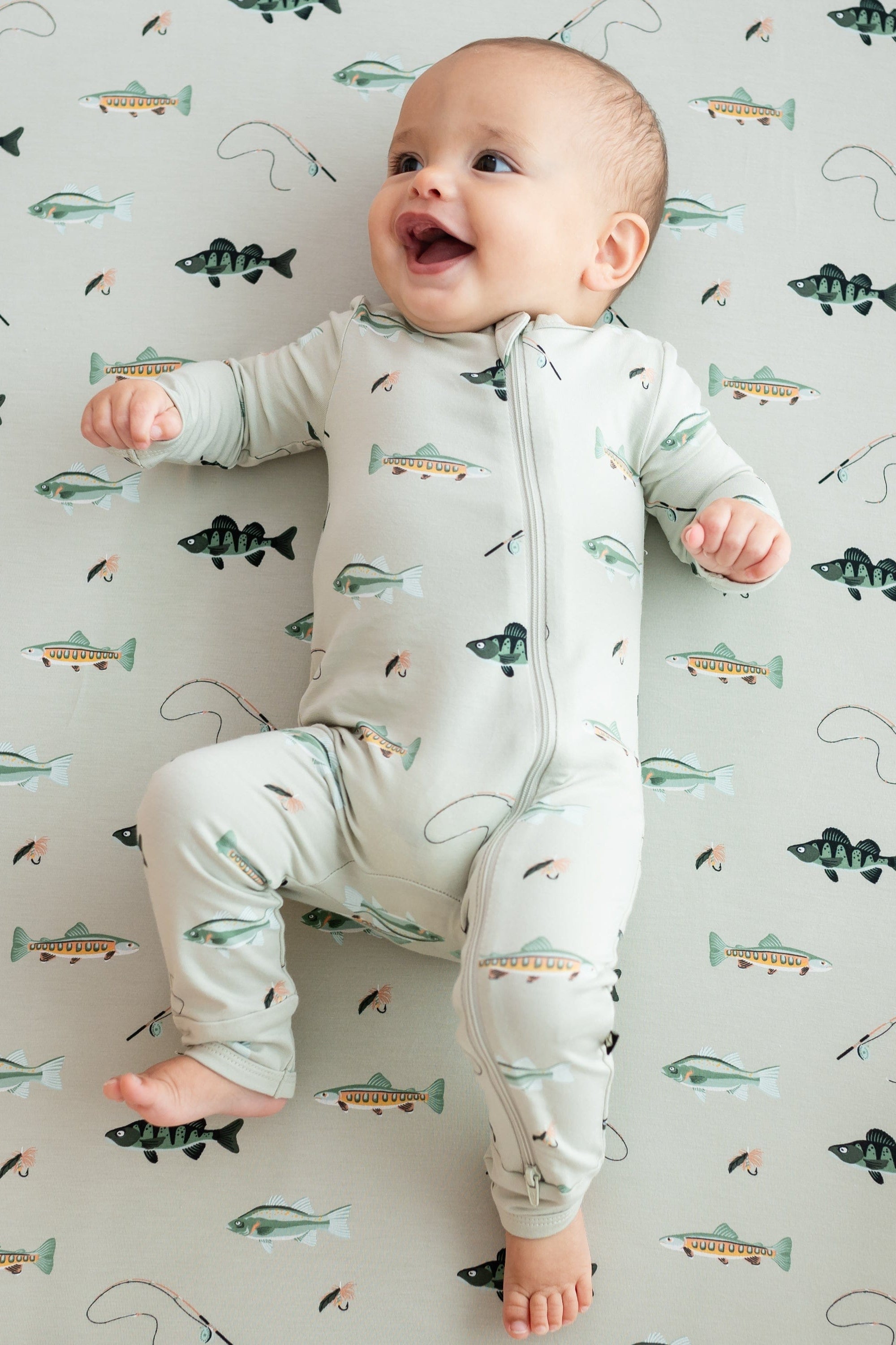 Smiling infant laying on a Fishing crib sheet wearing the Zippered Romper in Fishing