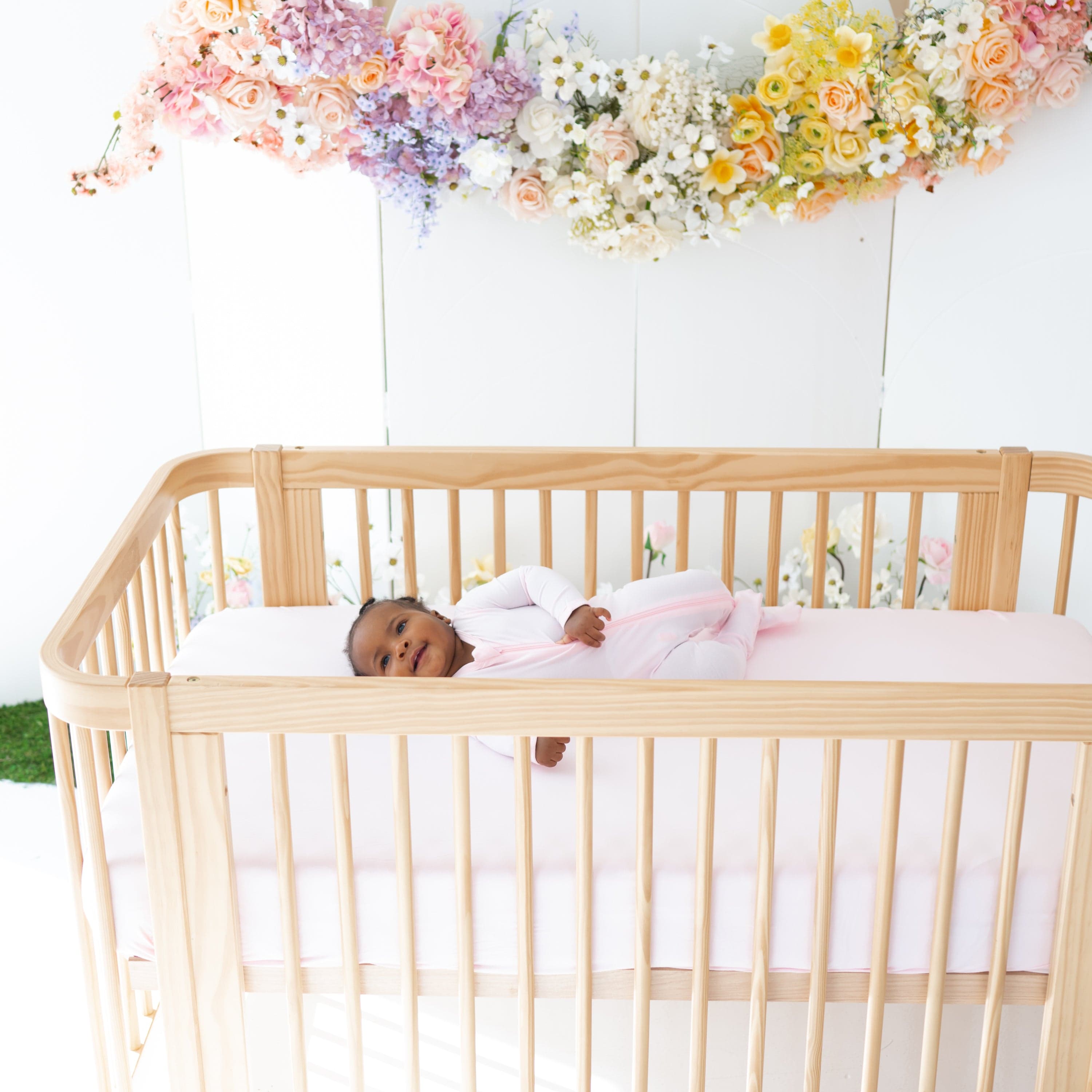 Infant laying on Kyte Baby Crib Sheet in Sakura pink