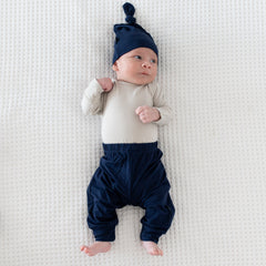 Newborn wearing Kyte Baby Knotted Cap in Navy with matching pants and a Long Sleeve Bodysuit in Oat
