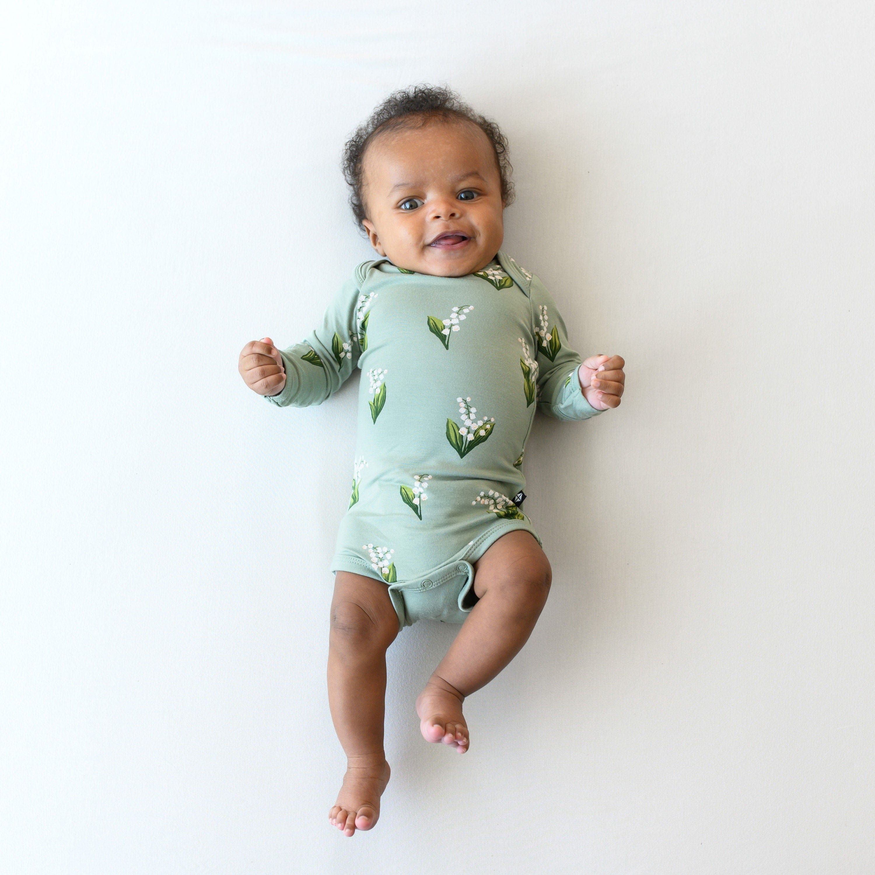 Infant wearing Kyte Baby Long Sleeve Bodysuit in Thyme Lily