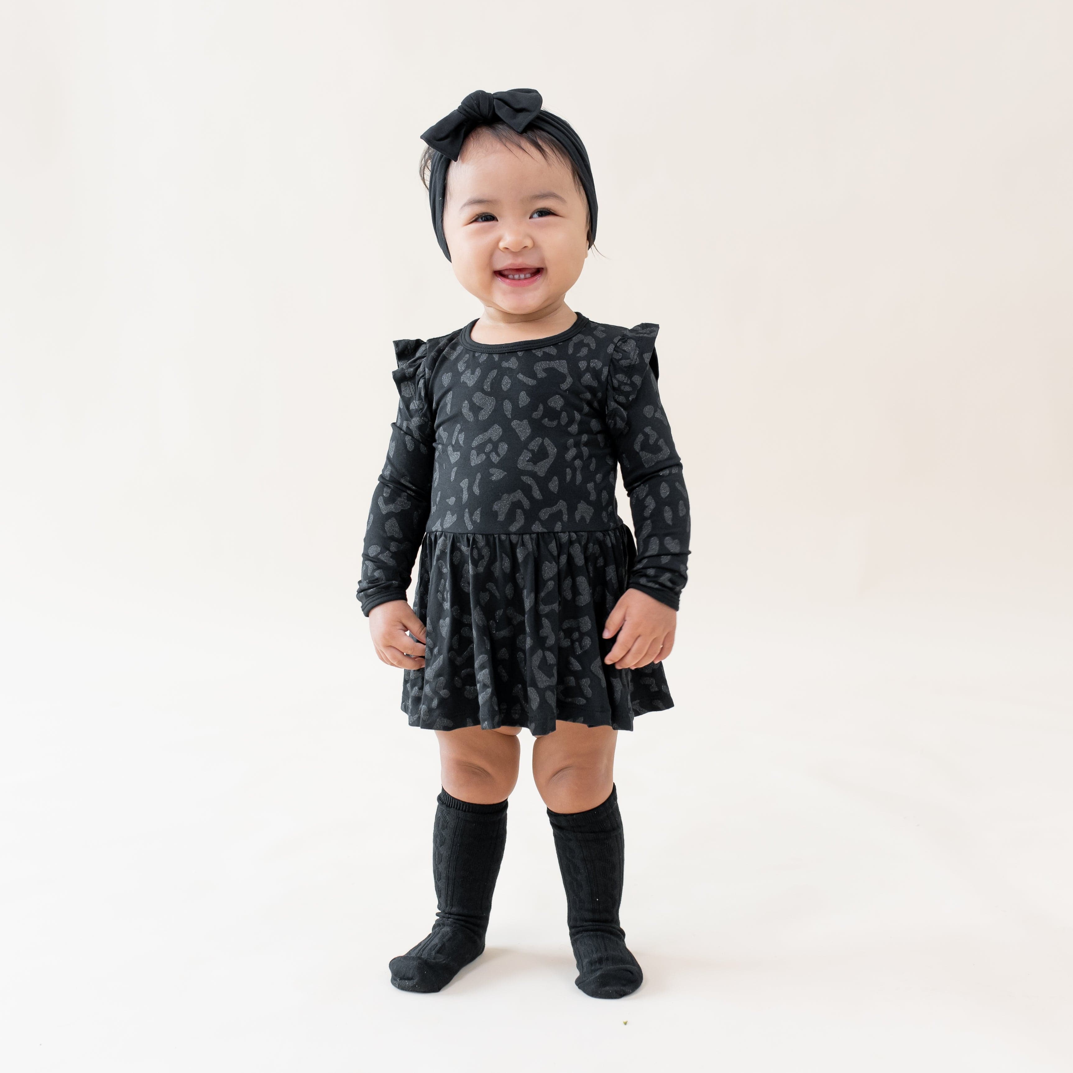 Infant wearing Kyte Baby Twirl Bodysuit Dress in Midnight Leopard