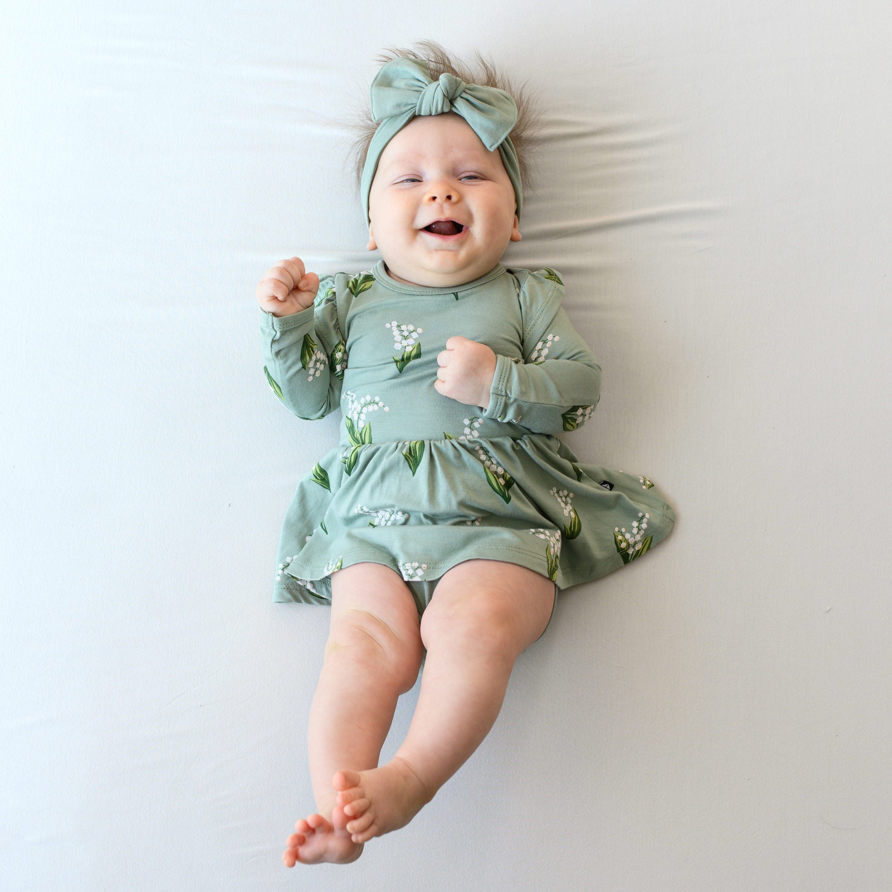 Infant wearing Kyte Baby Twirl Bodysuit Dress in Thyme Lily