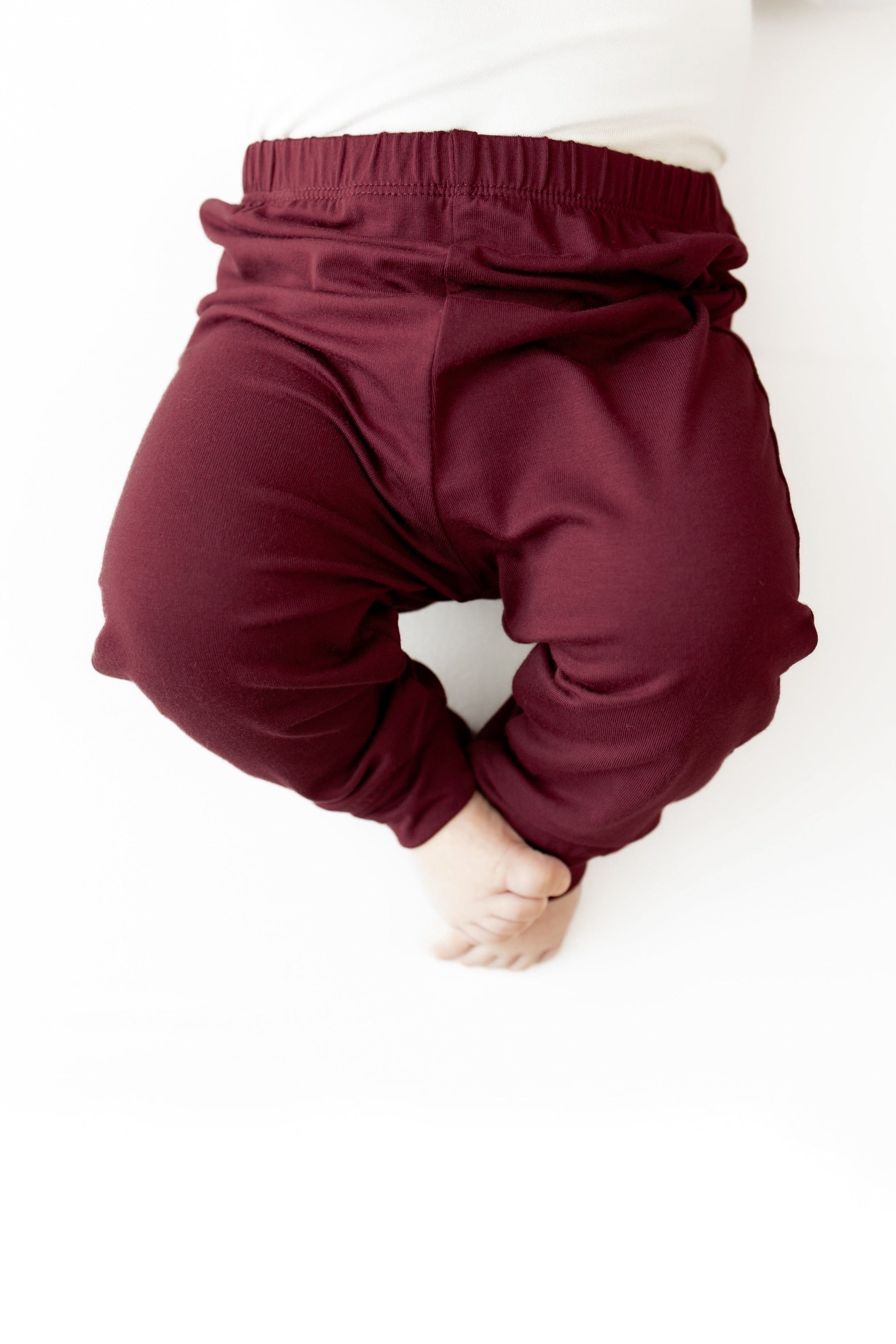 A close-up of a baby wearing burgundy elastic-waist pants, shown from the back against a plain white background.