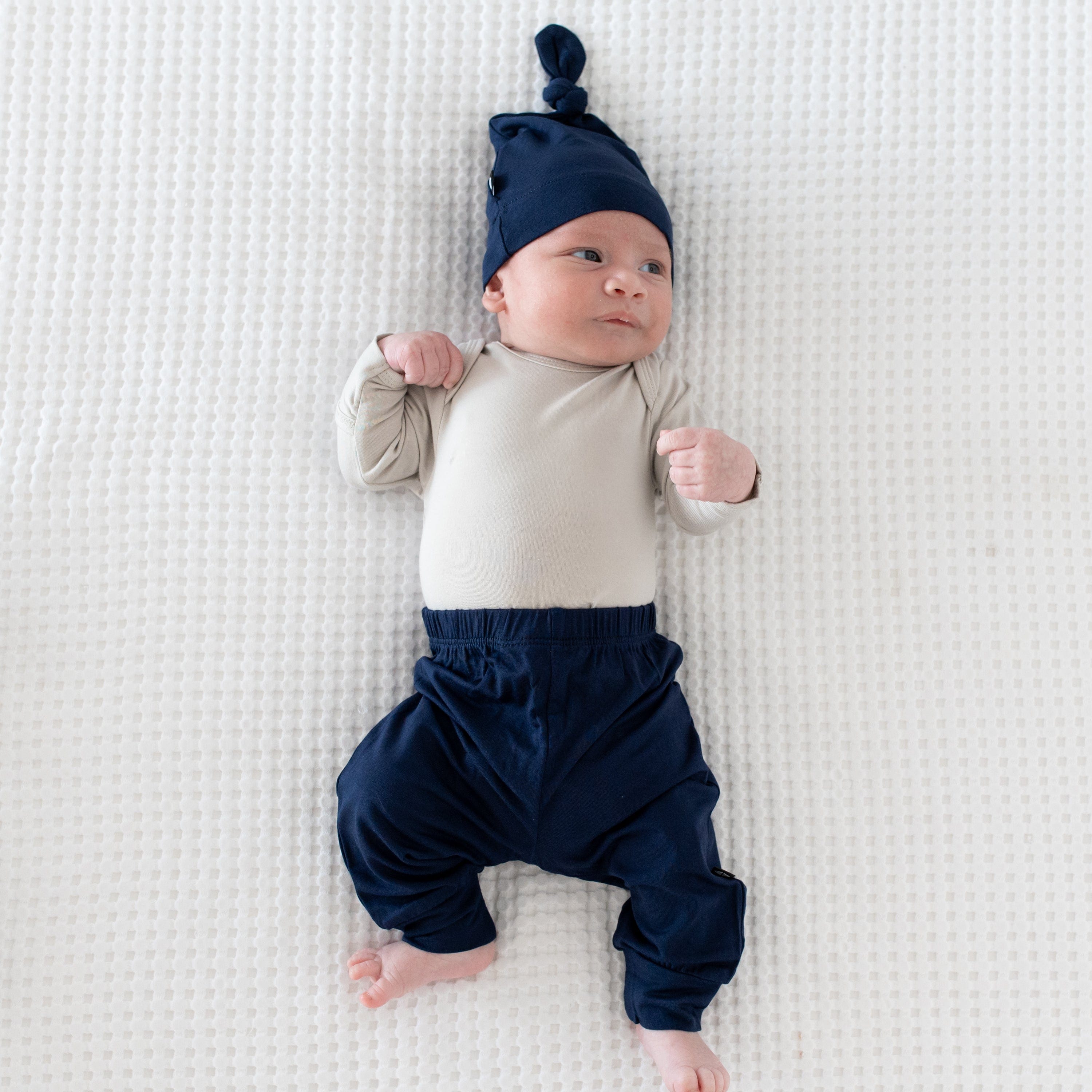 Newborn wearing a Kyte Baby Pant and Knotted Hat in Navy plus a long sleeve bodysuit in Oat