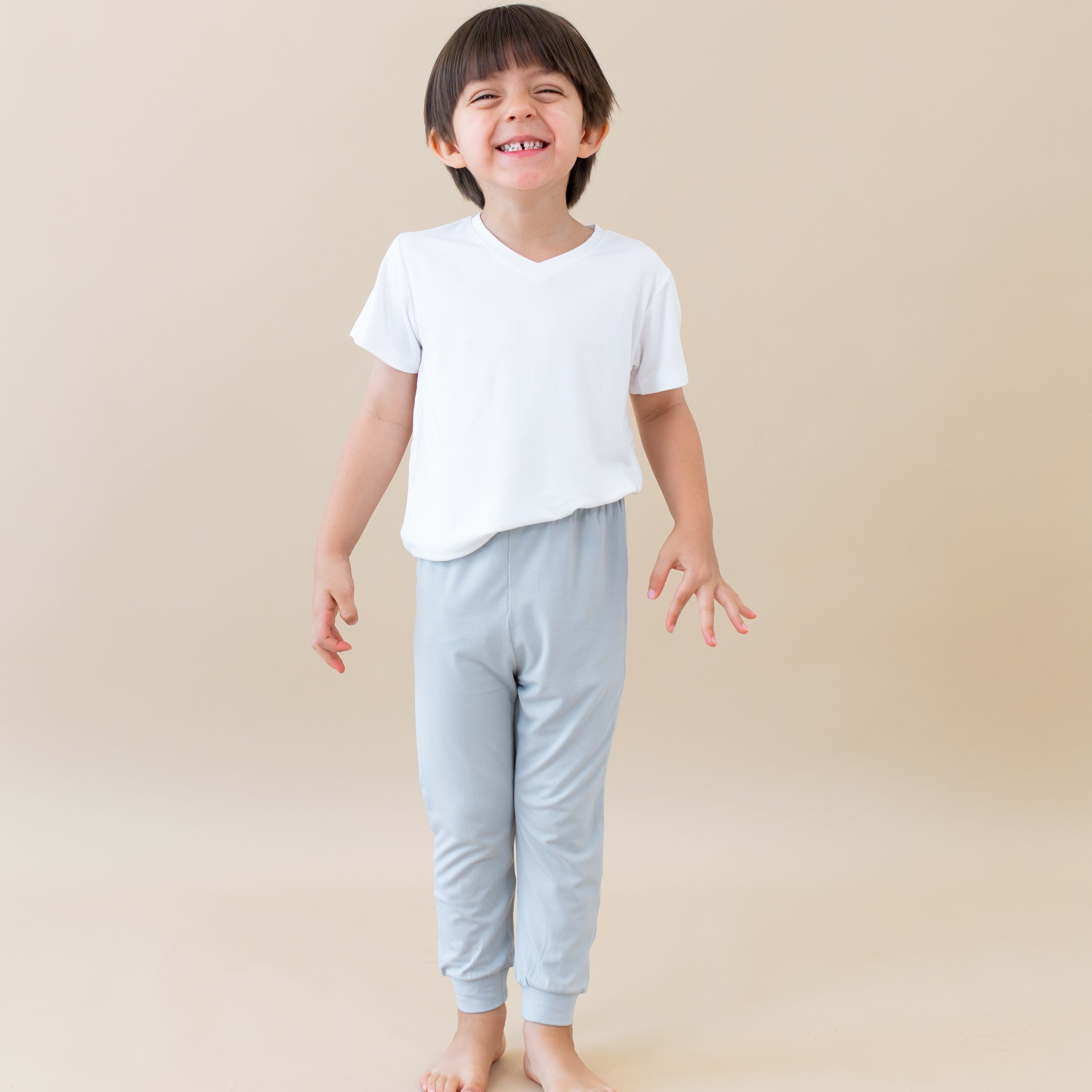 Smiling toddler standing while wearing Kyte Baby Pants in Storm and a V-Neck in Cloud