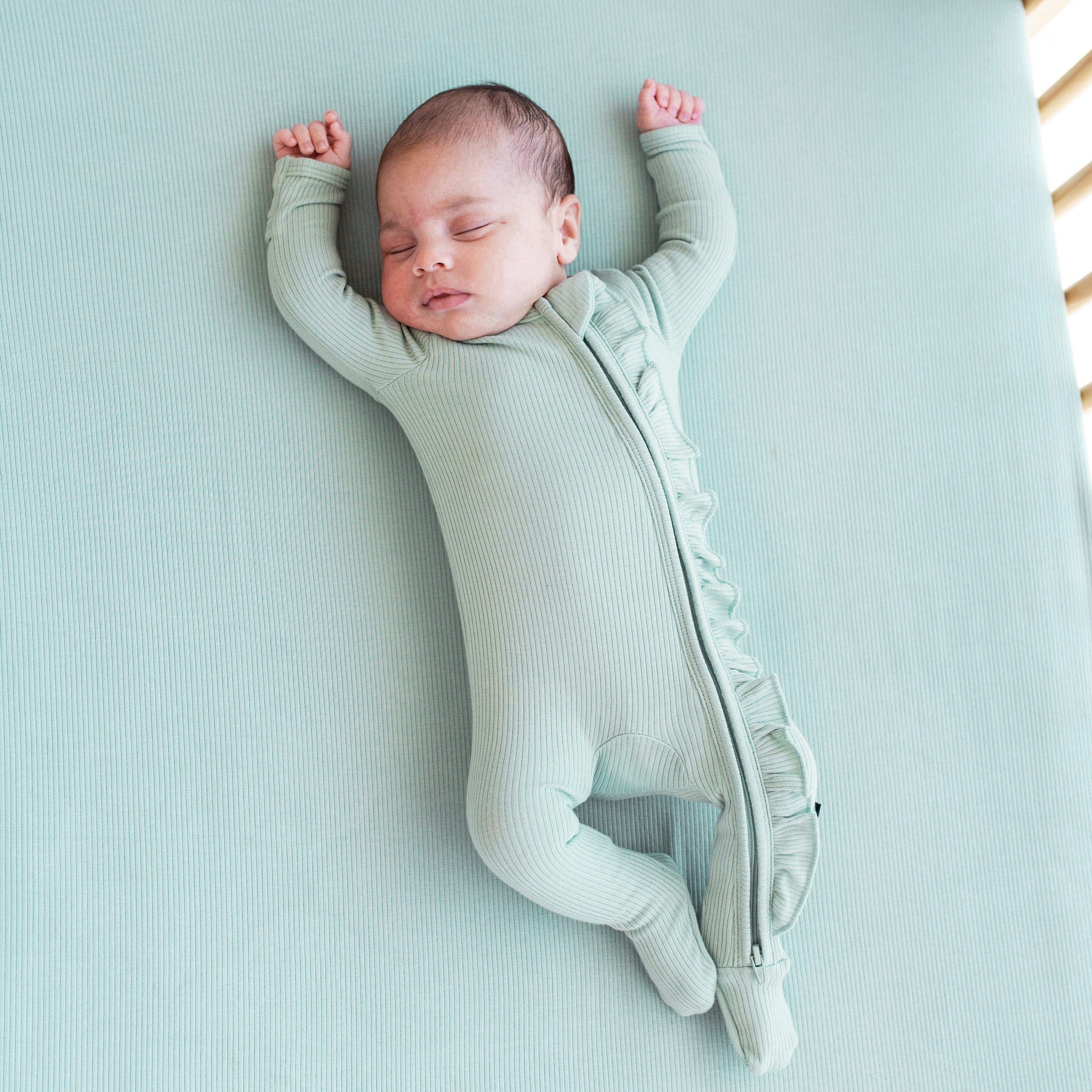 Newborn sleeping on Kyte Baby Ribbed Crib Sheet in Sage