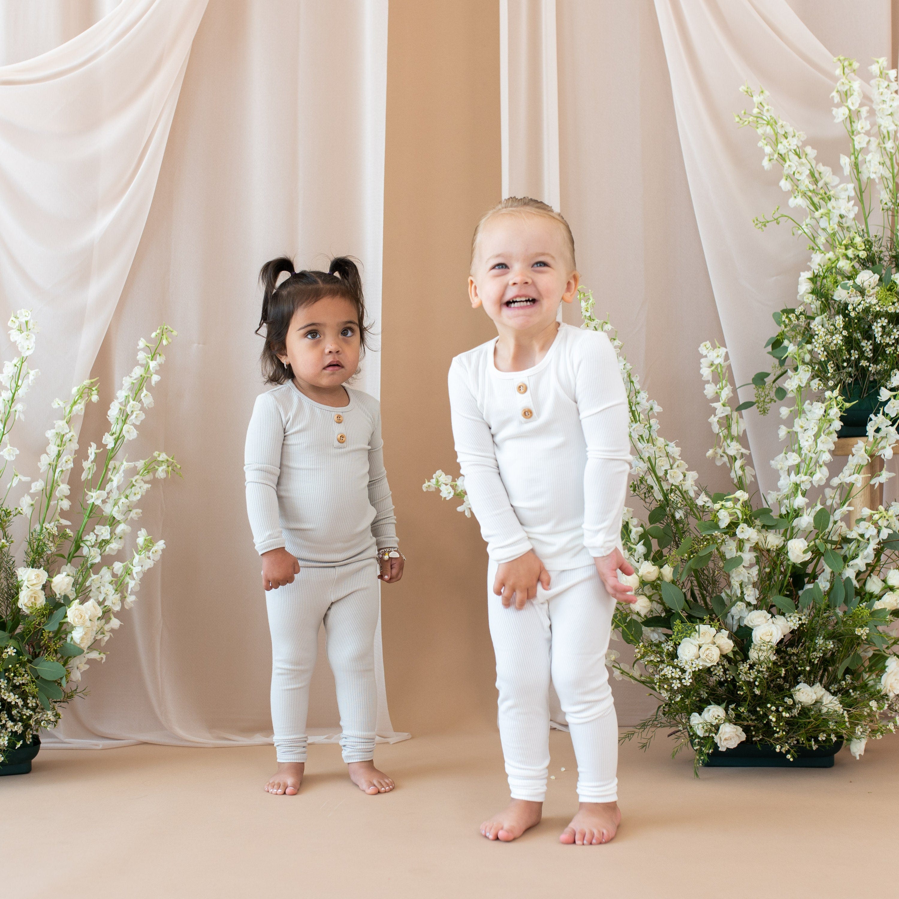 Two children wearing Kyte Baby Ribbed Henley Sets in Cloud and Oat
