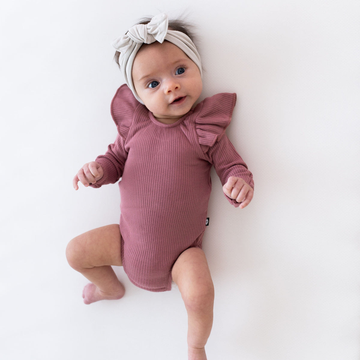 Newborn wearing Kyte Baby Ribbed Long Sleeve Ruffle Leotard in Dusty Rose