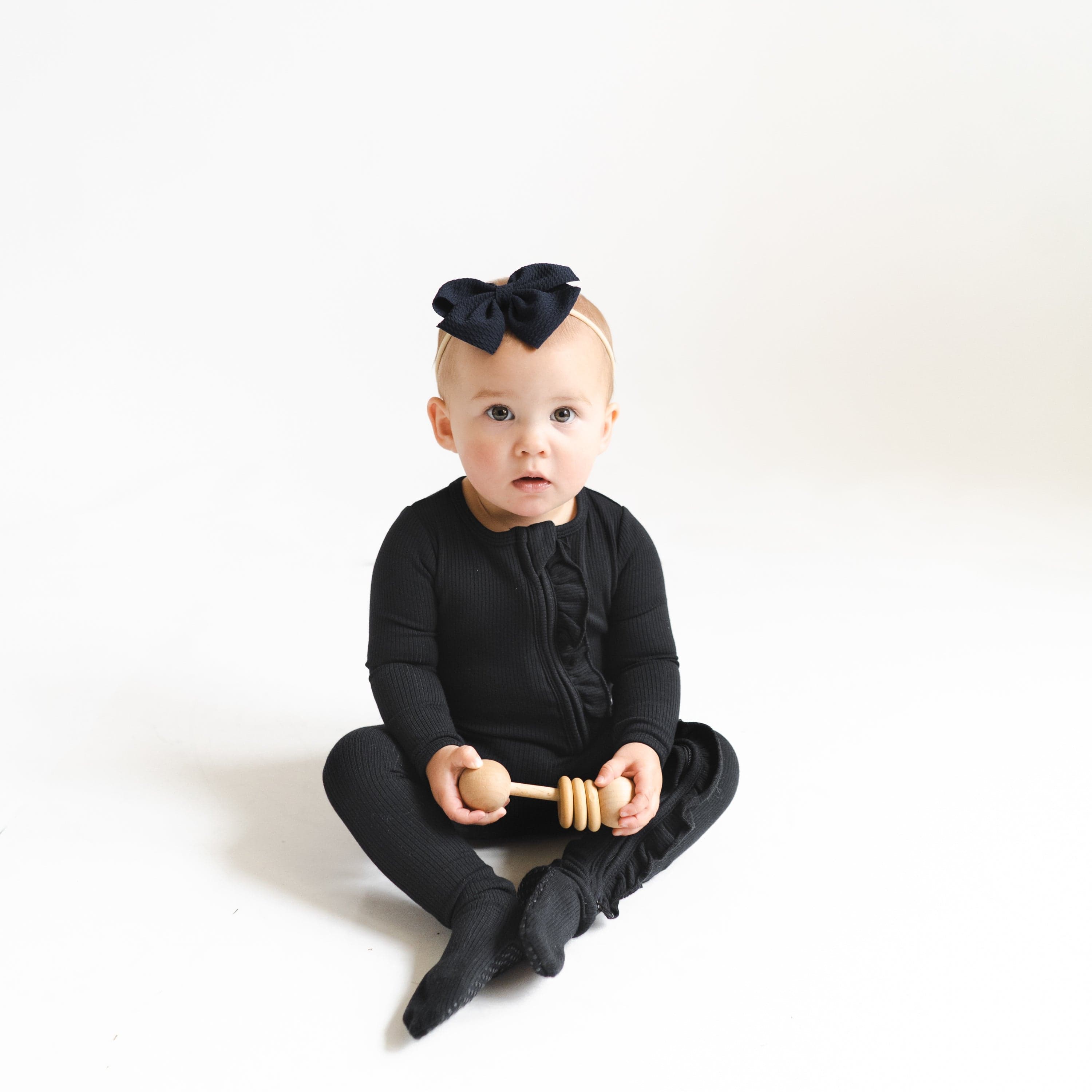 Girl wearing Kyte Baby bamboo Ribbed Ruffle Zipper Footie in Midnight