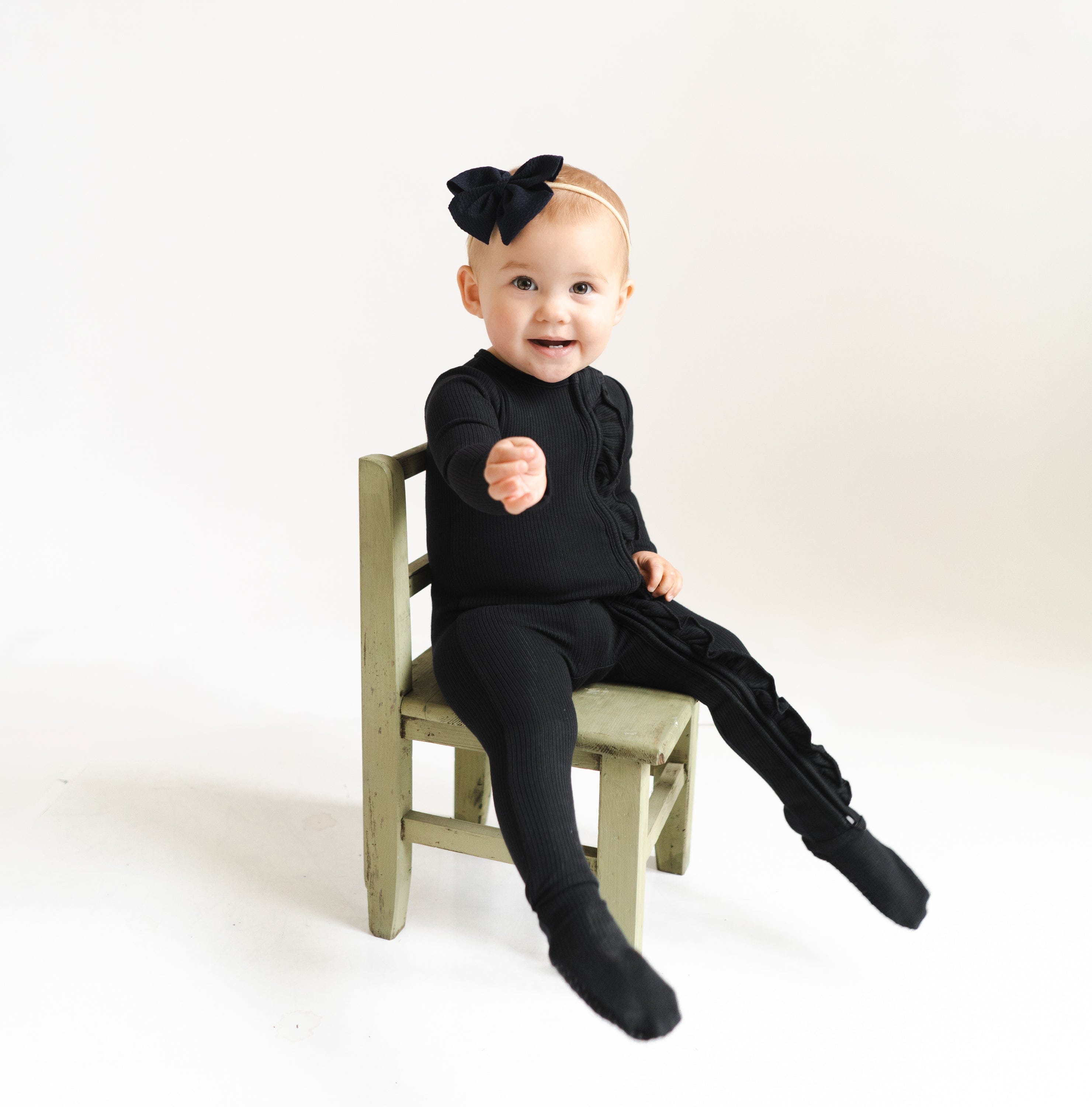 Toddler wearing Kyte Baby Ribbed Ruffle Zipper Footie in Midnight black