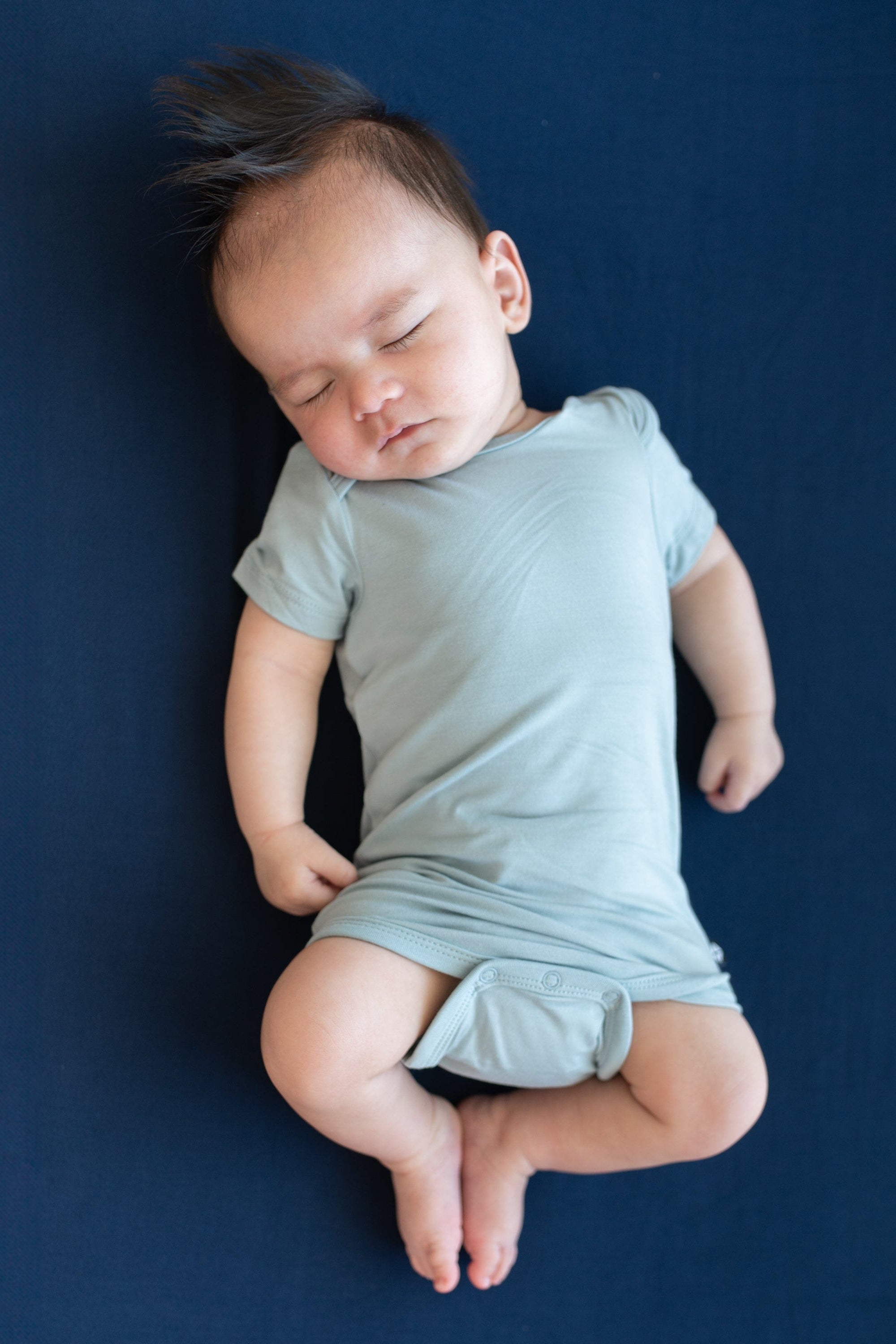 Sleeping baby laying on a Crib Sheet in Navy while wearing a Kyte Baby Bodysuit in Fog