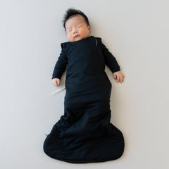 Sleeping infant in Kyte Baby Sleep Bag in Midnight 1.0 and a matching long sleeve bodysuit underneath 