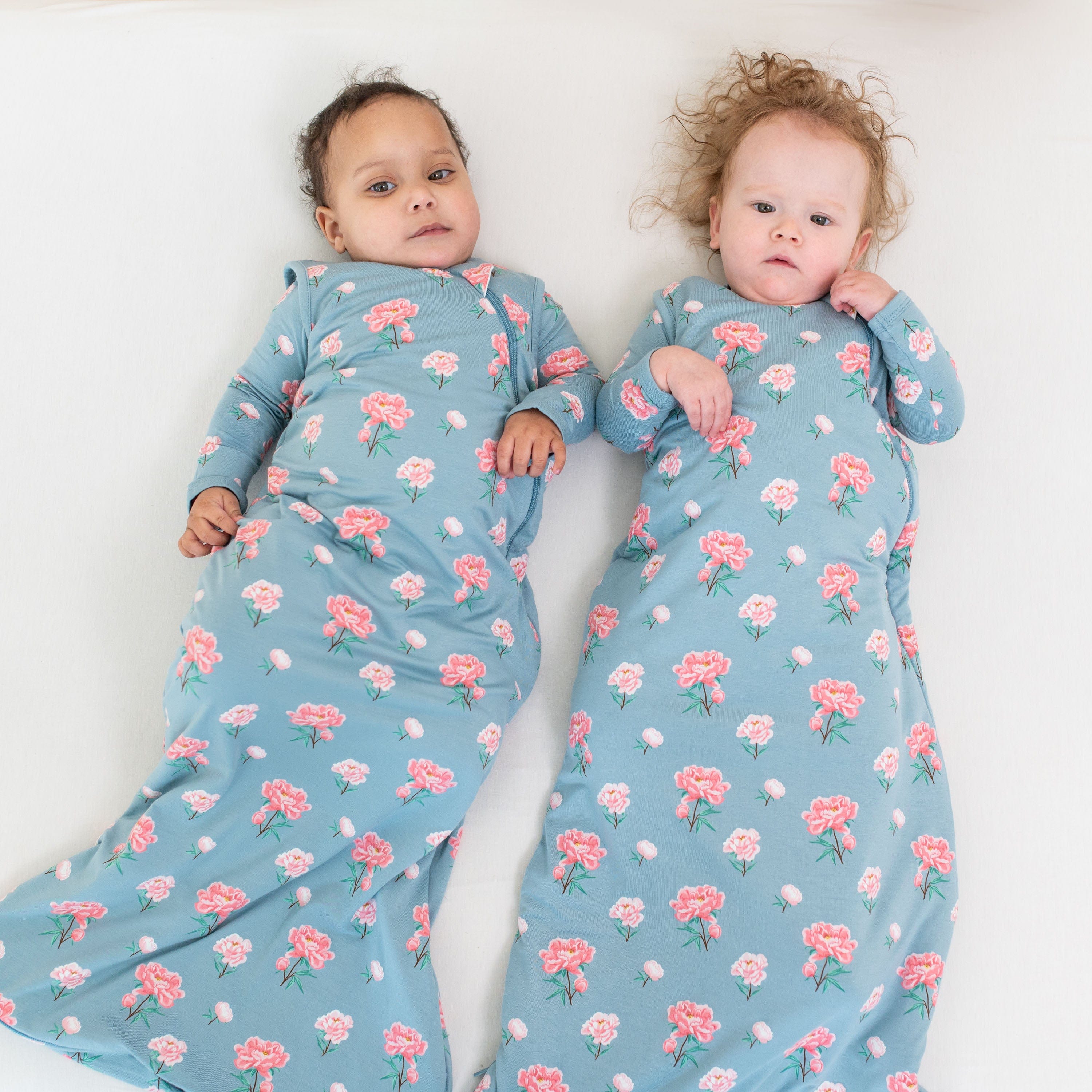 Babies wearing Kyte Baby sleep bags TOG 1.0 in Peony pattern
