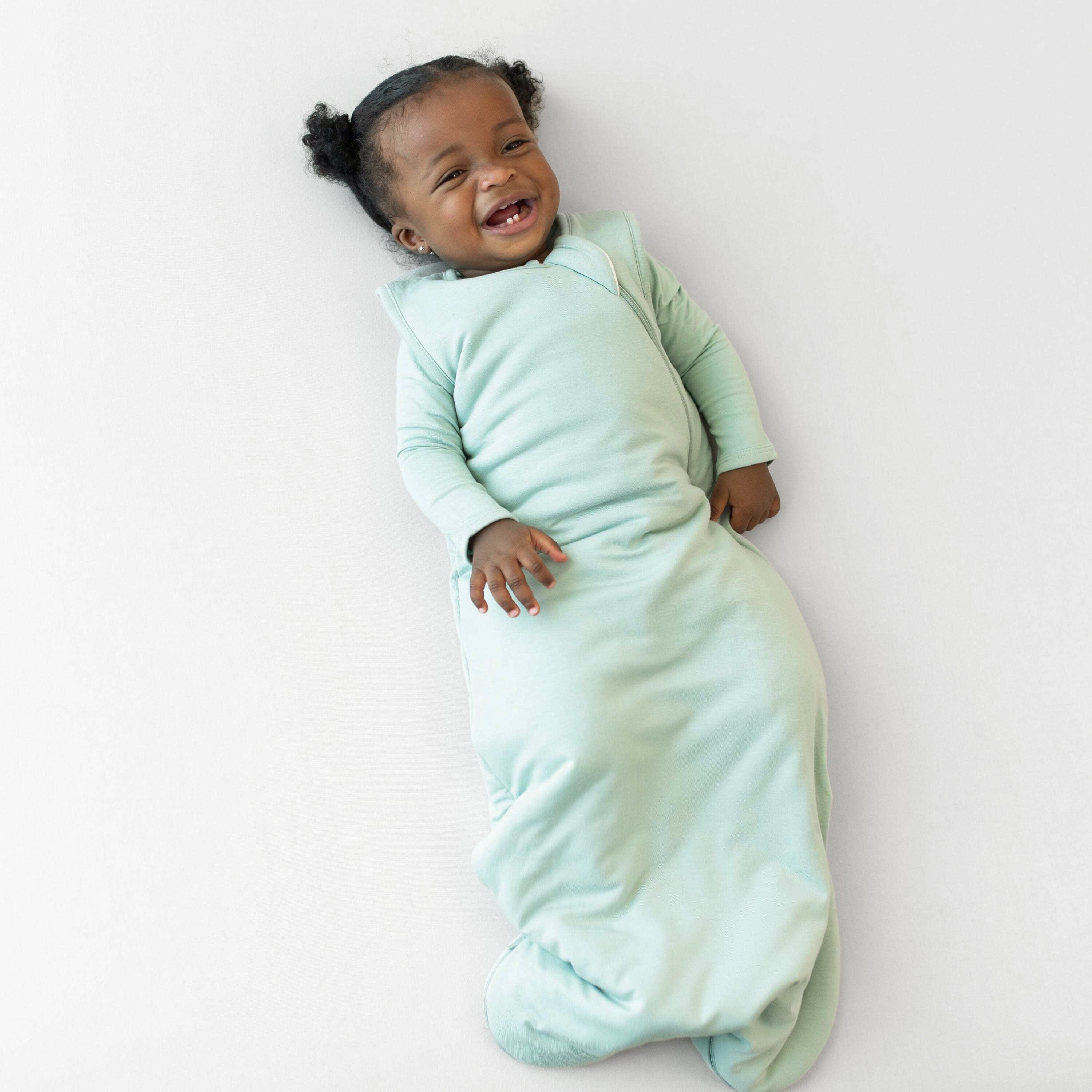 Baby in a cozy sage green wearable balnket on a white background