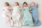 Four infants laying next to each other wearing 1.0 Sleep Bags in core colors - Blush, Oat, Sage, Slate.