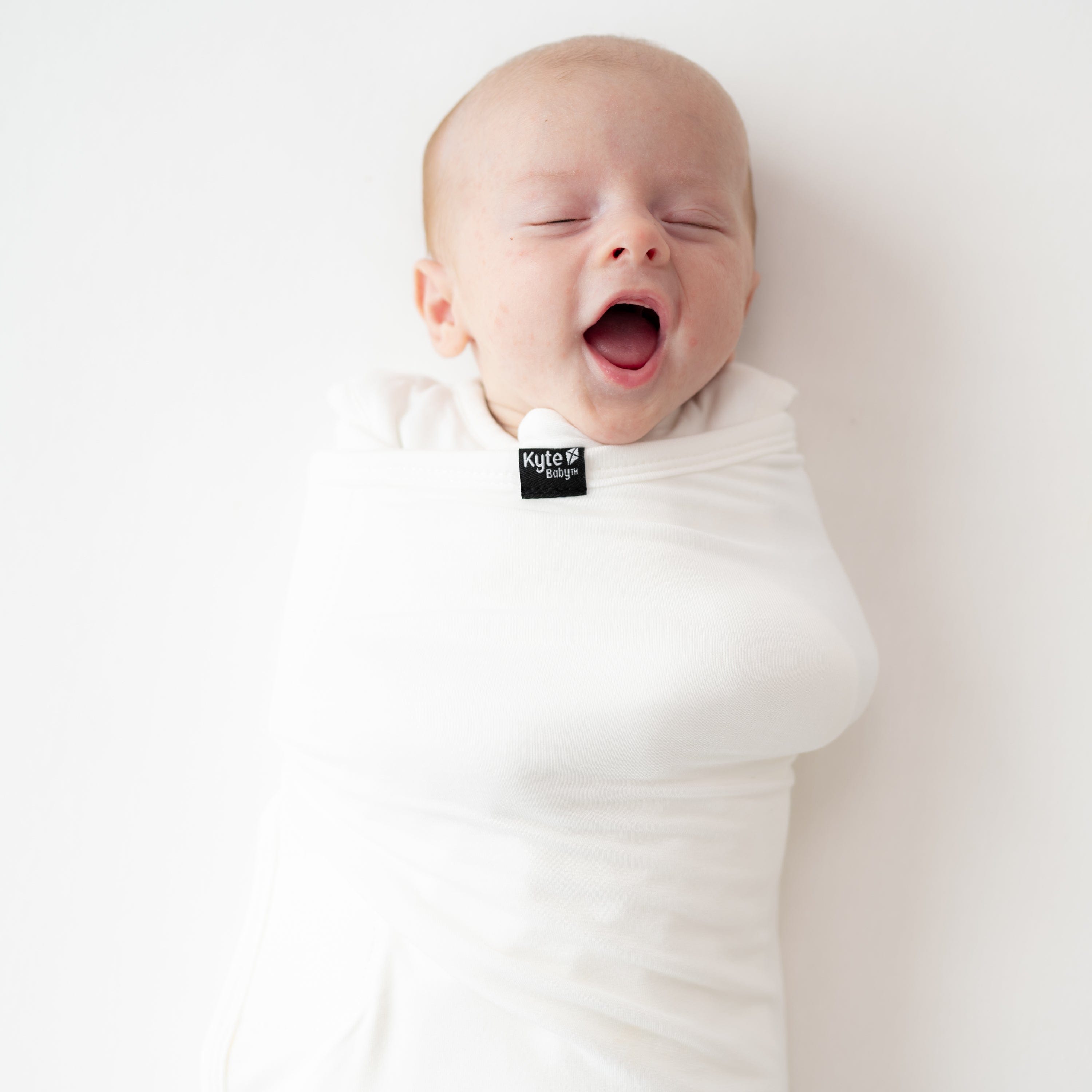 Baby yawning and wearing Kyte Baby Sleep Bag Swaddler in Cloud