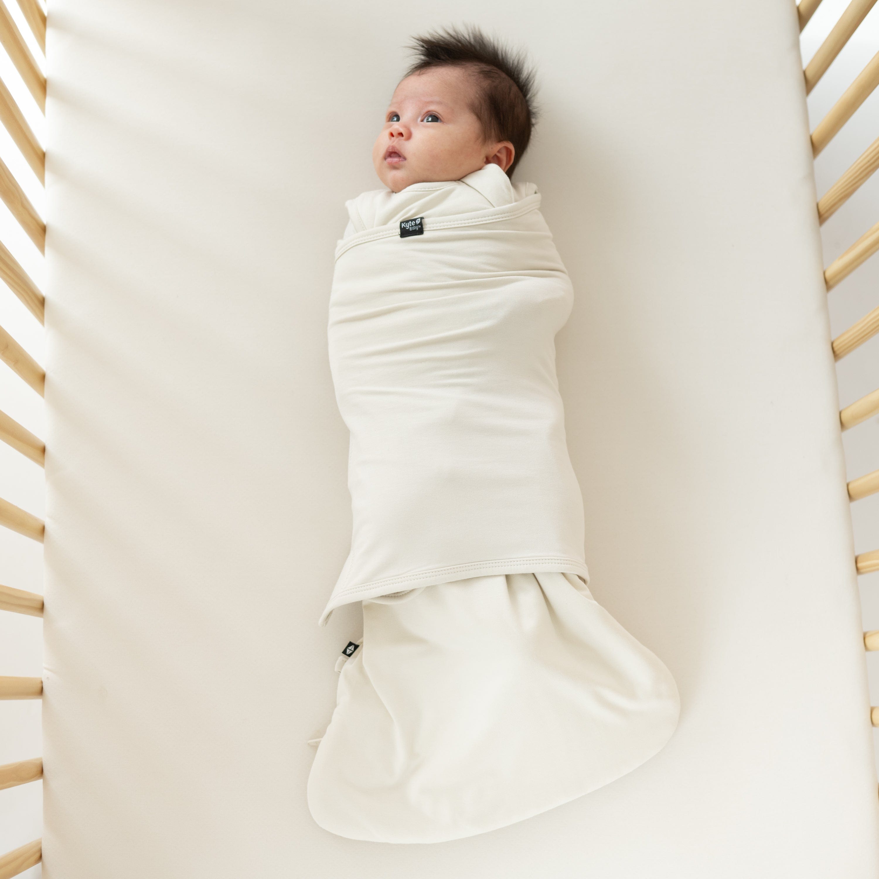 Newborn wearing Kyte Baby Sleep Bag Swaddler in Ecru with elastic band