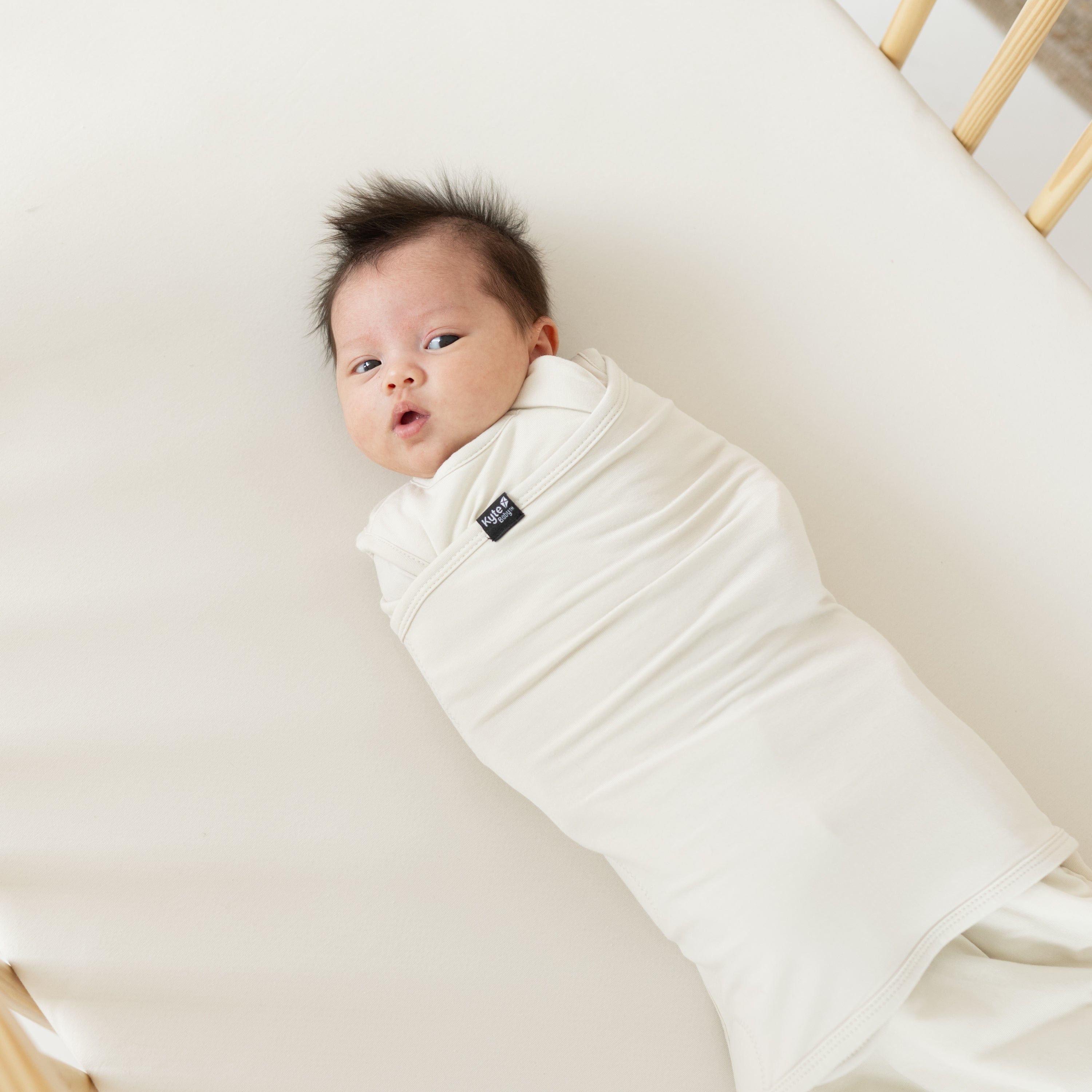 Infant wearing Kyte Baby Sleep Bag Swaddler in Ecru with elastic band