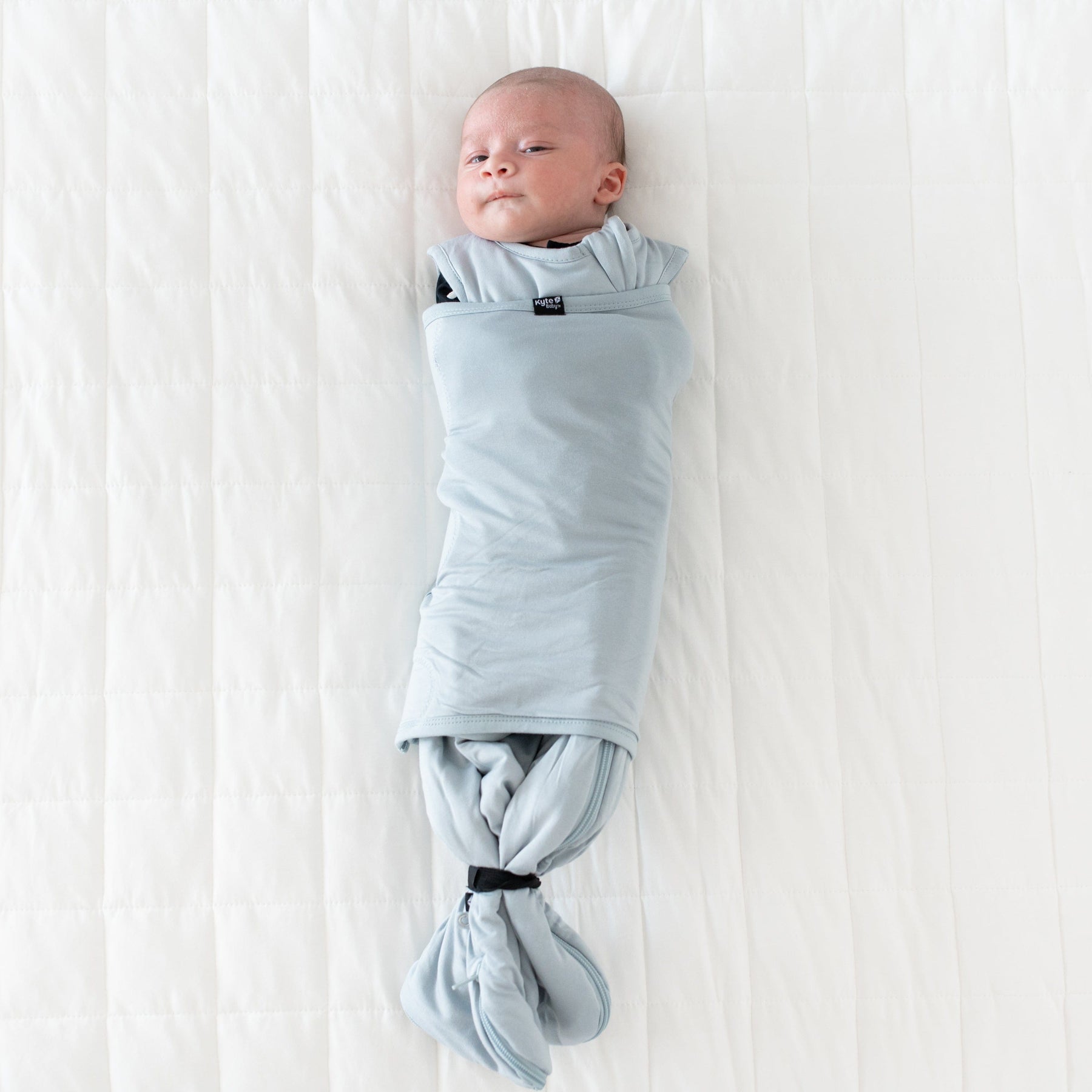 Baby wearing Kyte Baby Sleep Bag with swaddle band and elastic tie in Fog