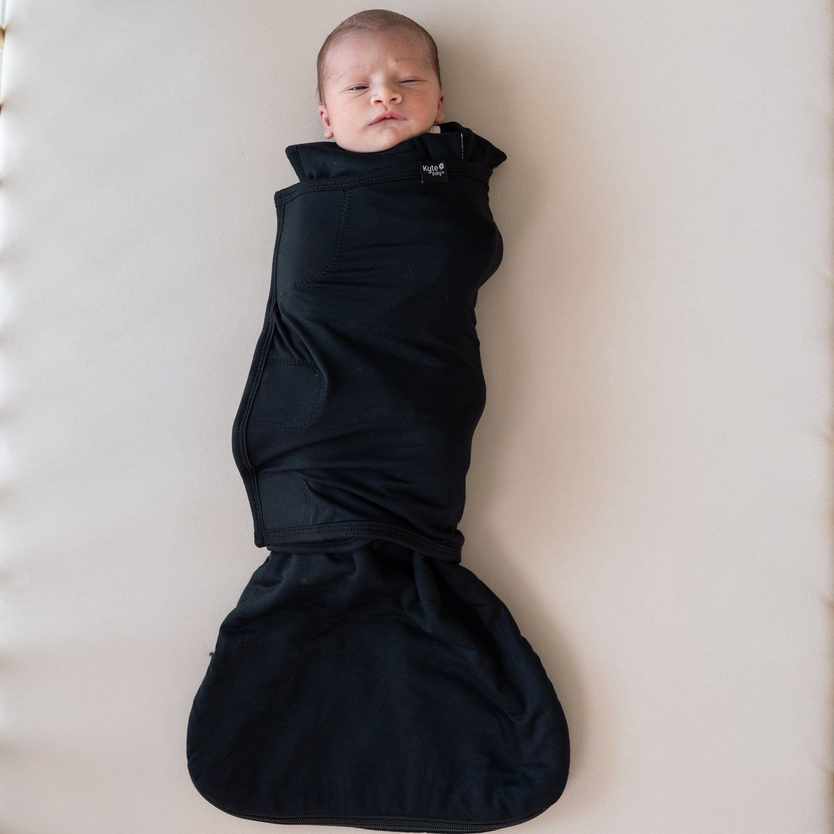 Baby wearing Kyte Baby Sleep Bag Swaddler in Midnight black