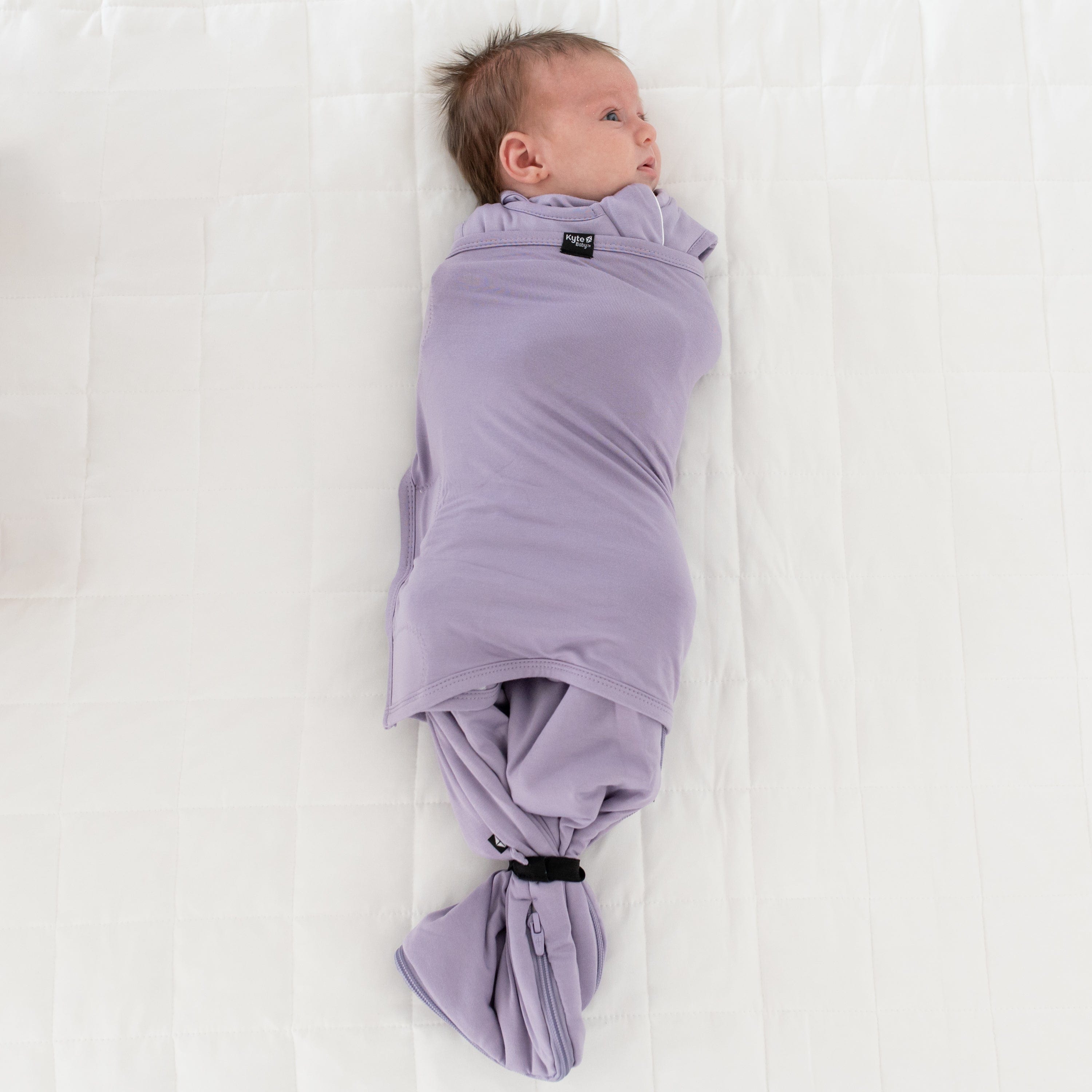 Baby wearing Kyte Baby Sleep Bag Swaddler in Taro with elastic band