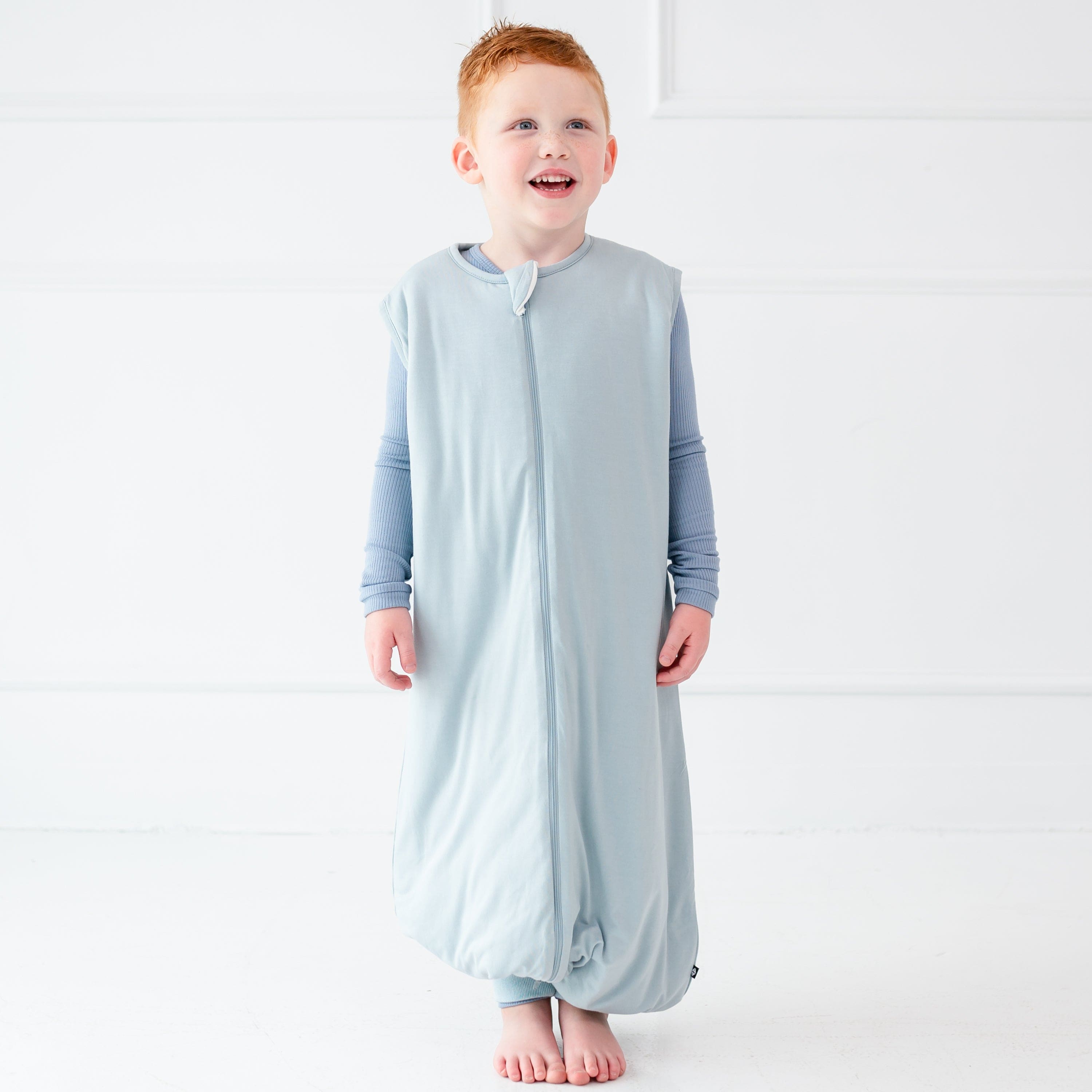 Standing child wearing the Sleep Bag Walker in Fog 1.0 with long sleeve pajama set in Slate underneath