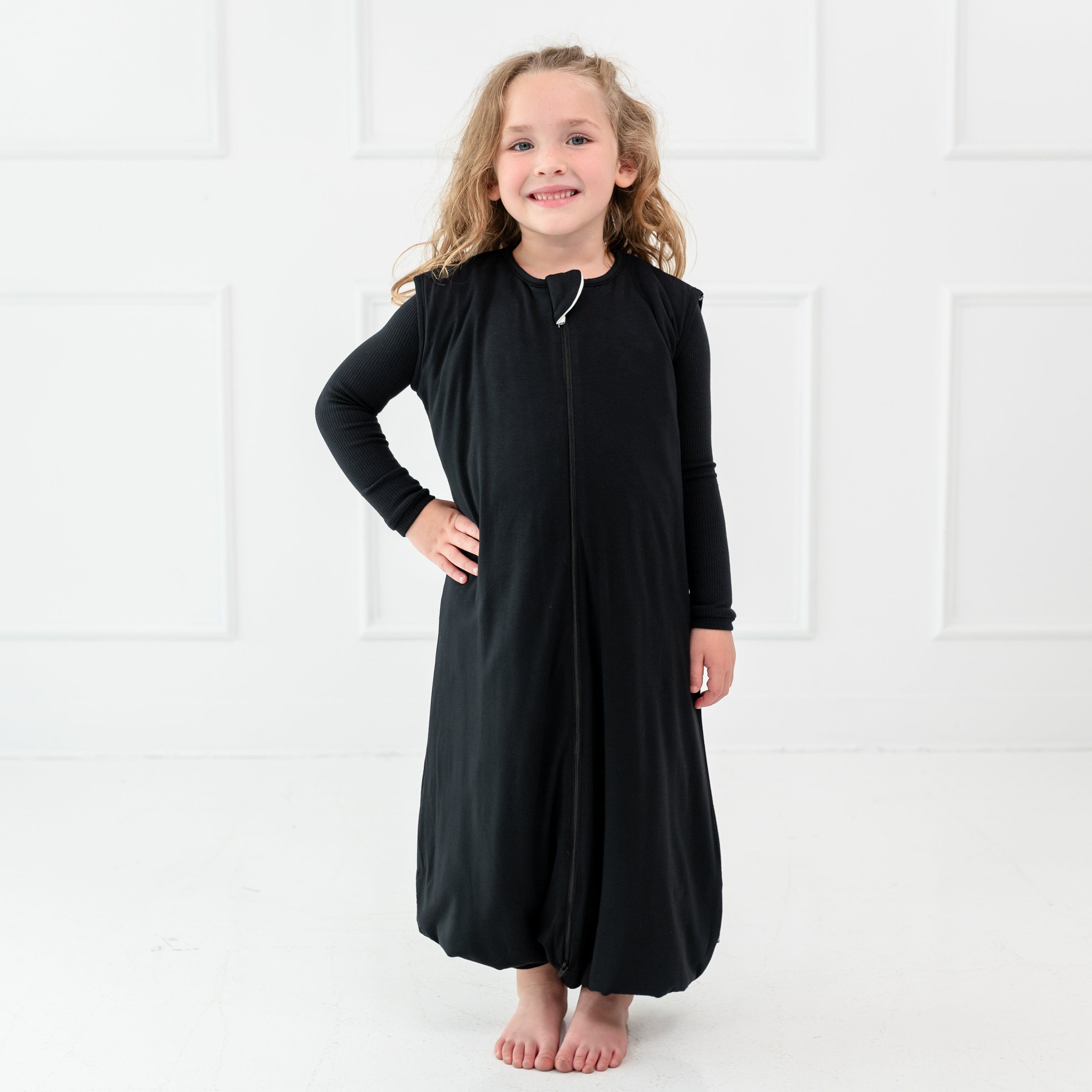 Girl model standing infront of whilte wall while wearing Sleep Bag Walker in Midnight 1.0 with one hand on her waist