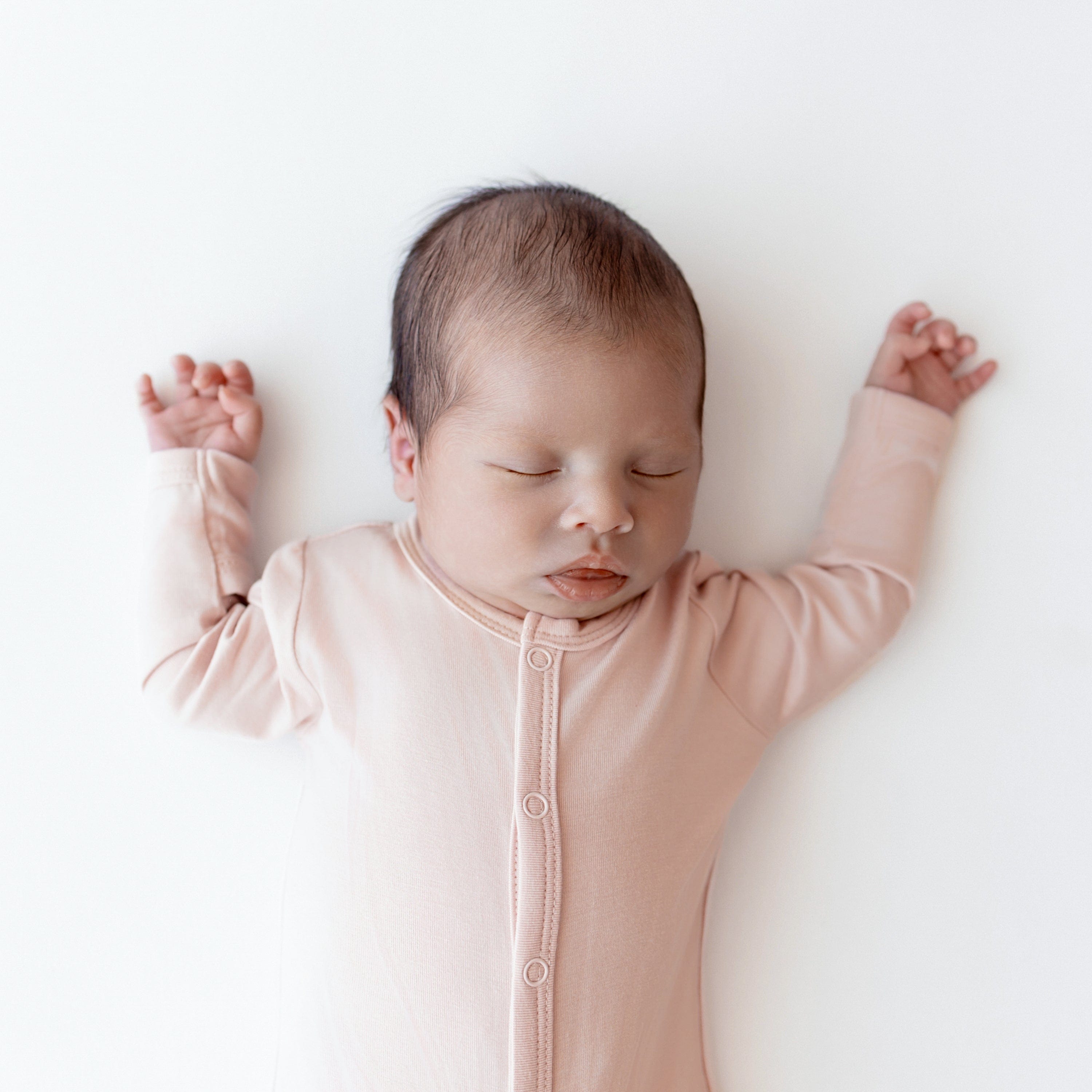 Close up of sleeping infant wearing Kyte Baby Footie in Blush with arms up