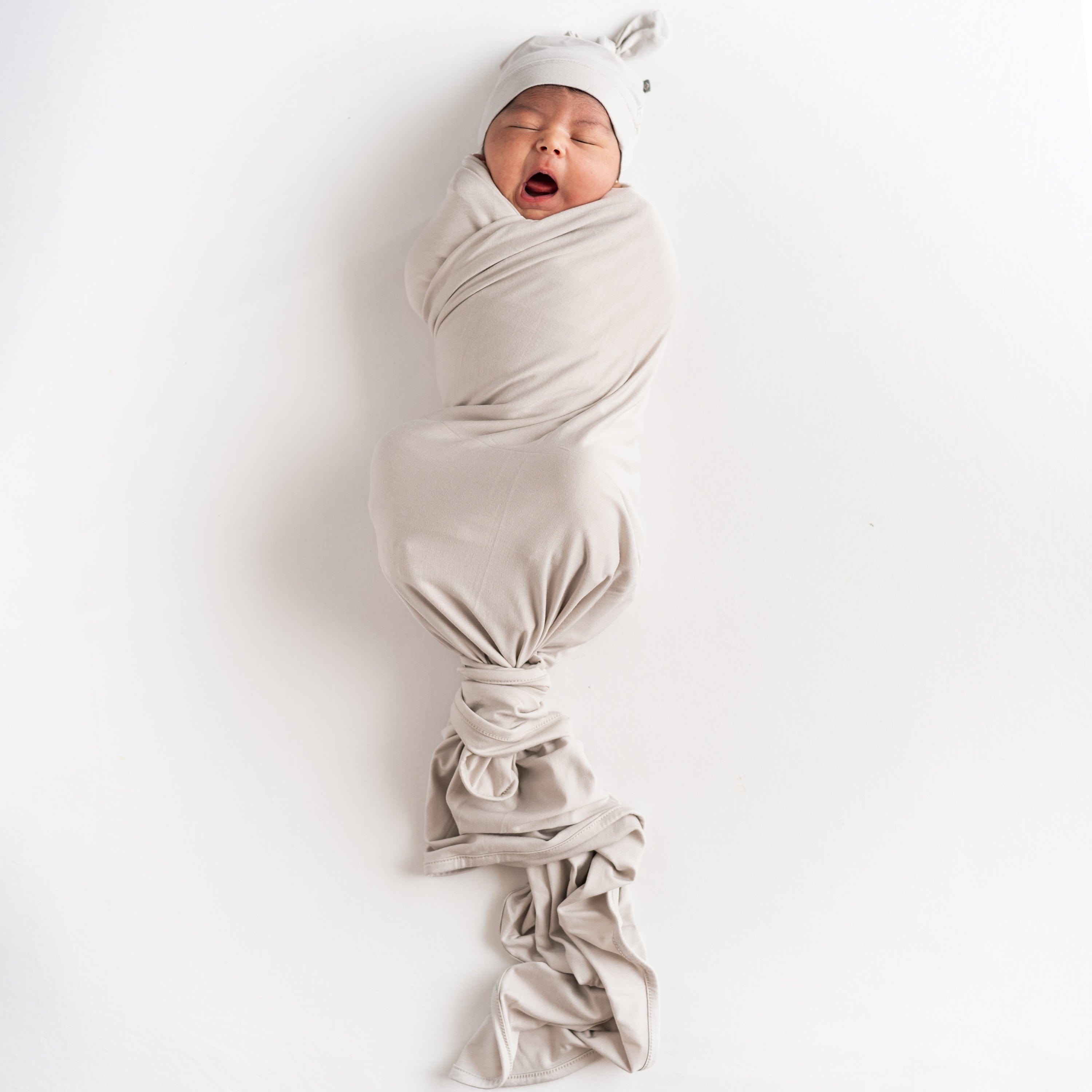 Newborn sleeping in Kyte Baby Swaddle Blanket in Oat