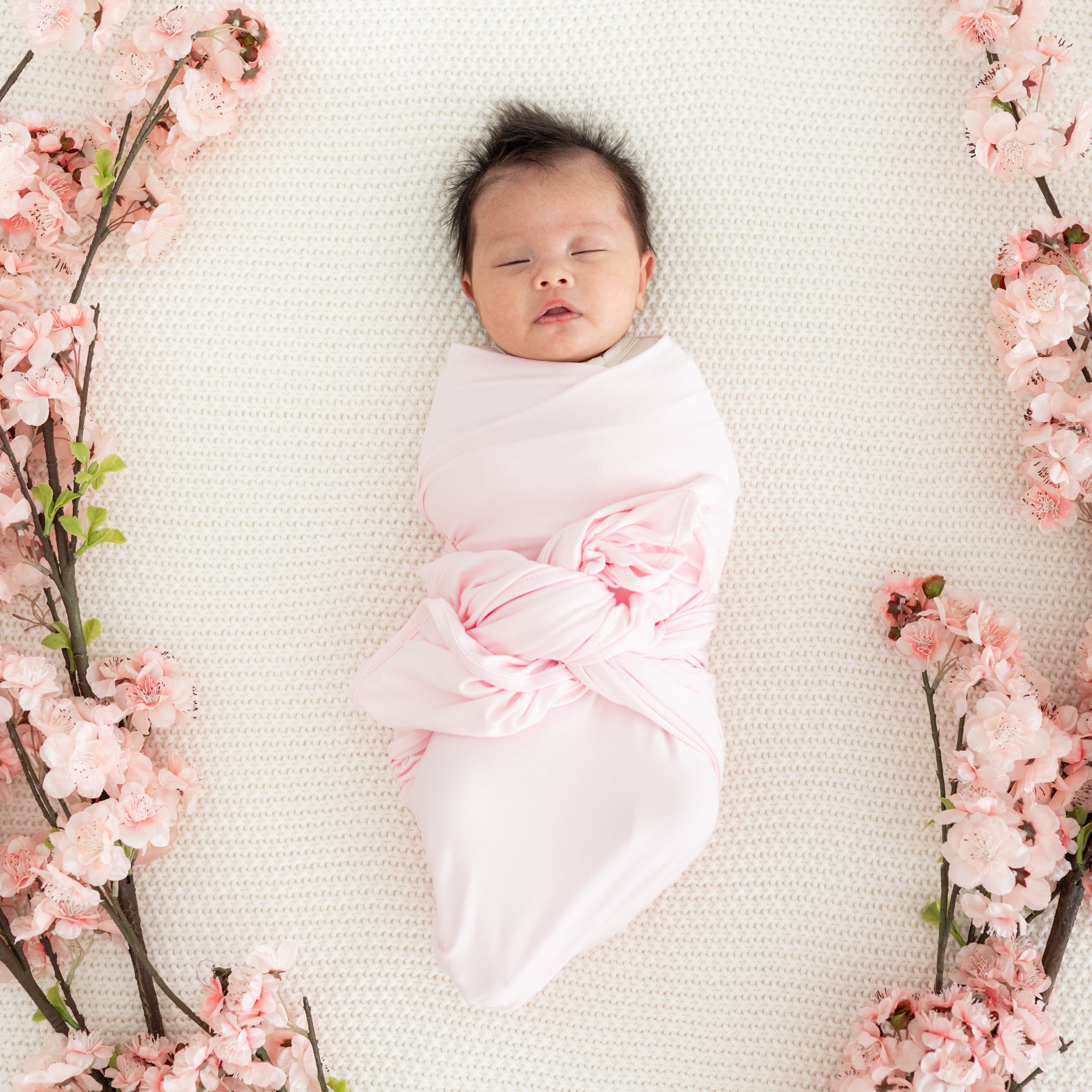 Newborn sleeping in Kyte Baby Swaddle Blanket in Sakura